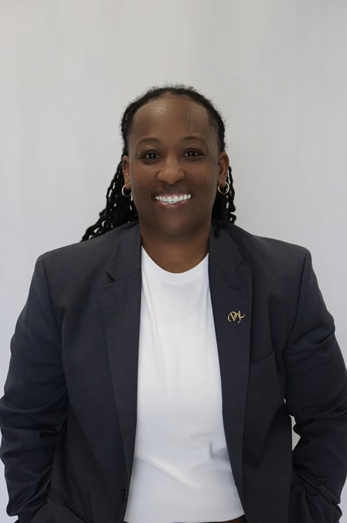 Woman in a dark blazer and white shirt smiling, standing against a plain background.