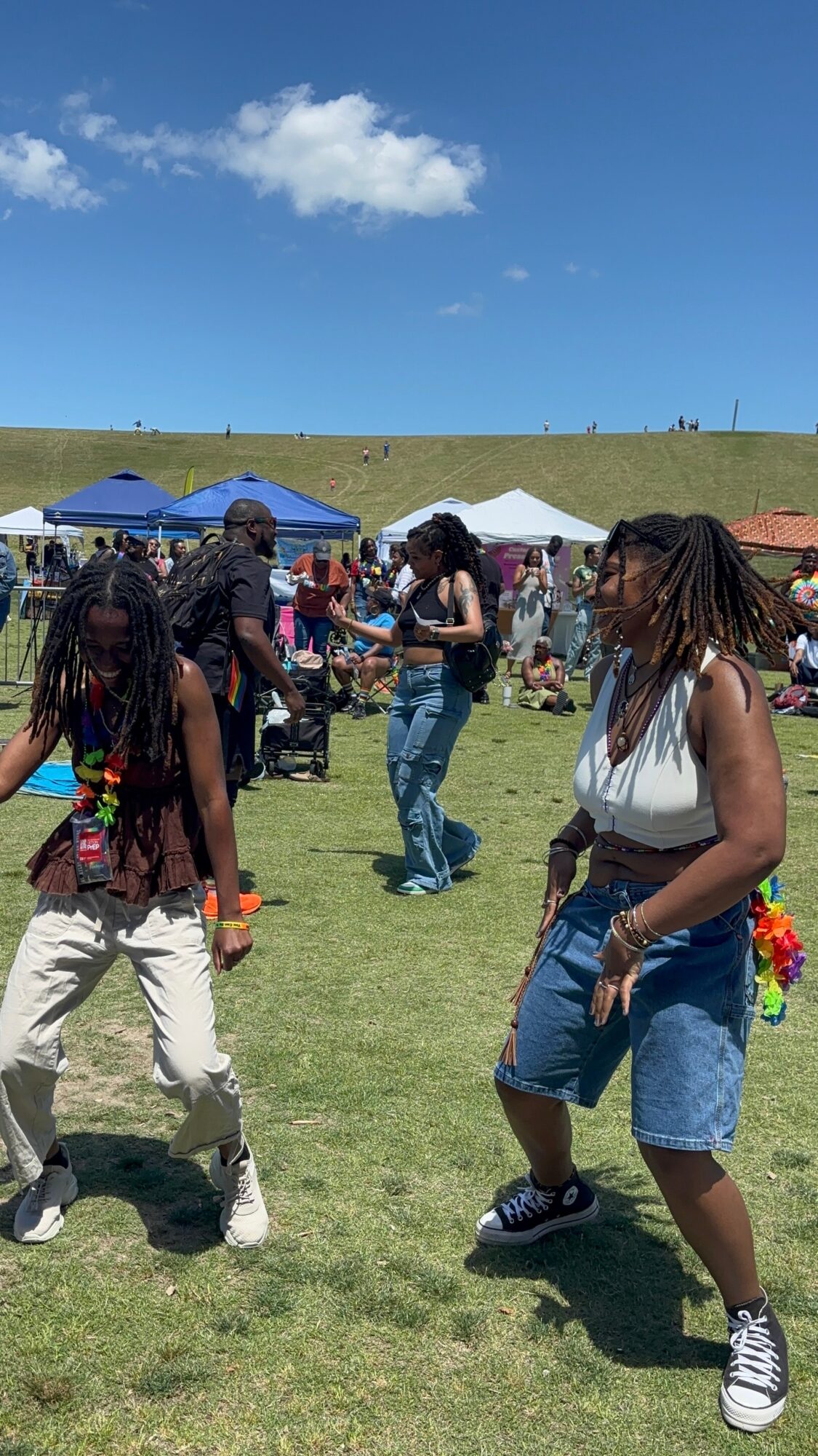 People dancing outdoors on grass with tents and a blue sky in the background.