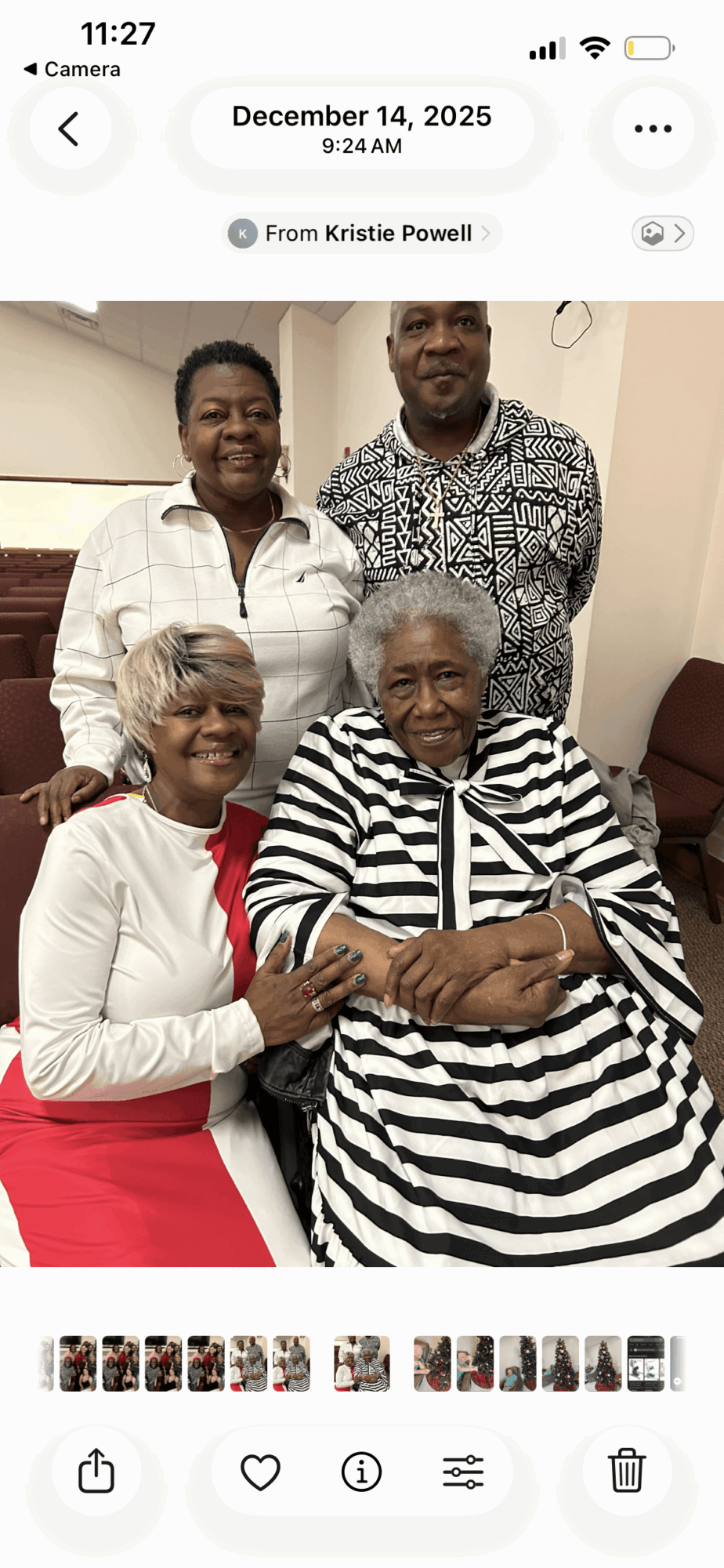 Four people, two women and two men, smiling and sitting together indoors, one woman in a striped dress, others in casual clothing.