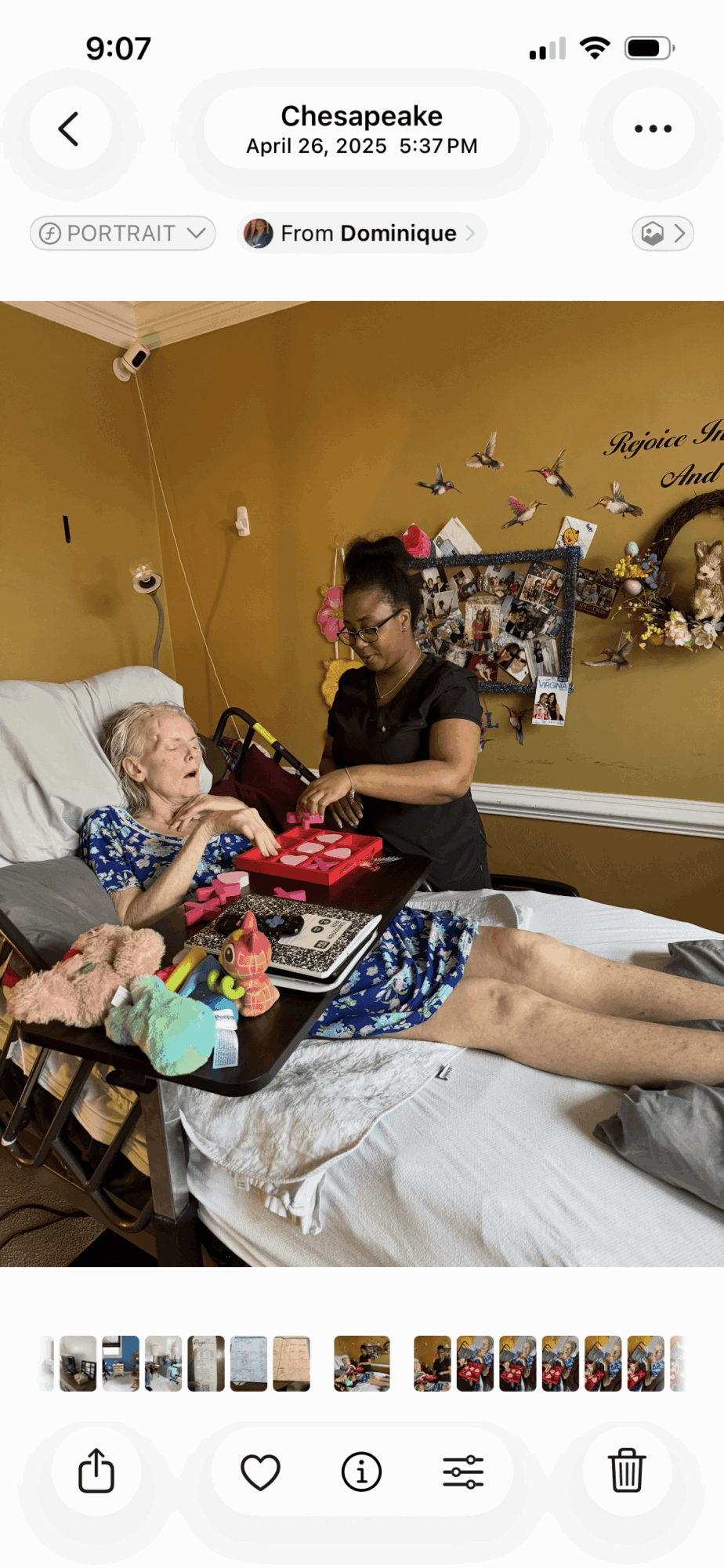 Person in hospital bed with a young girl, woman standing nearby, yellow wall with decorations in background