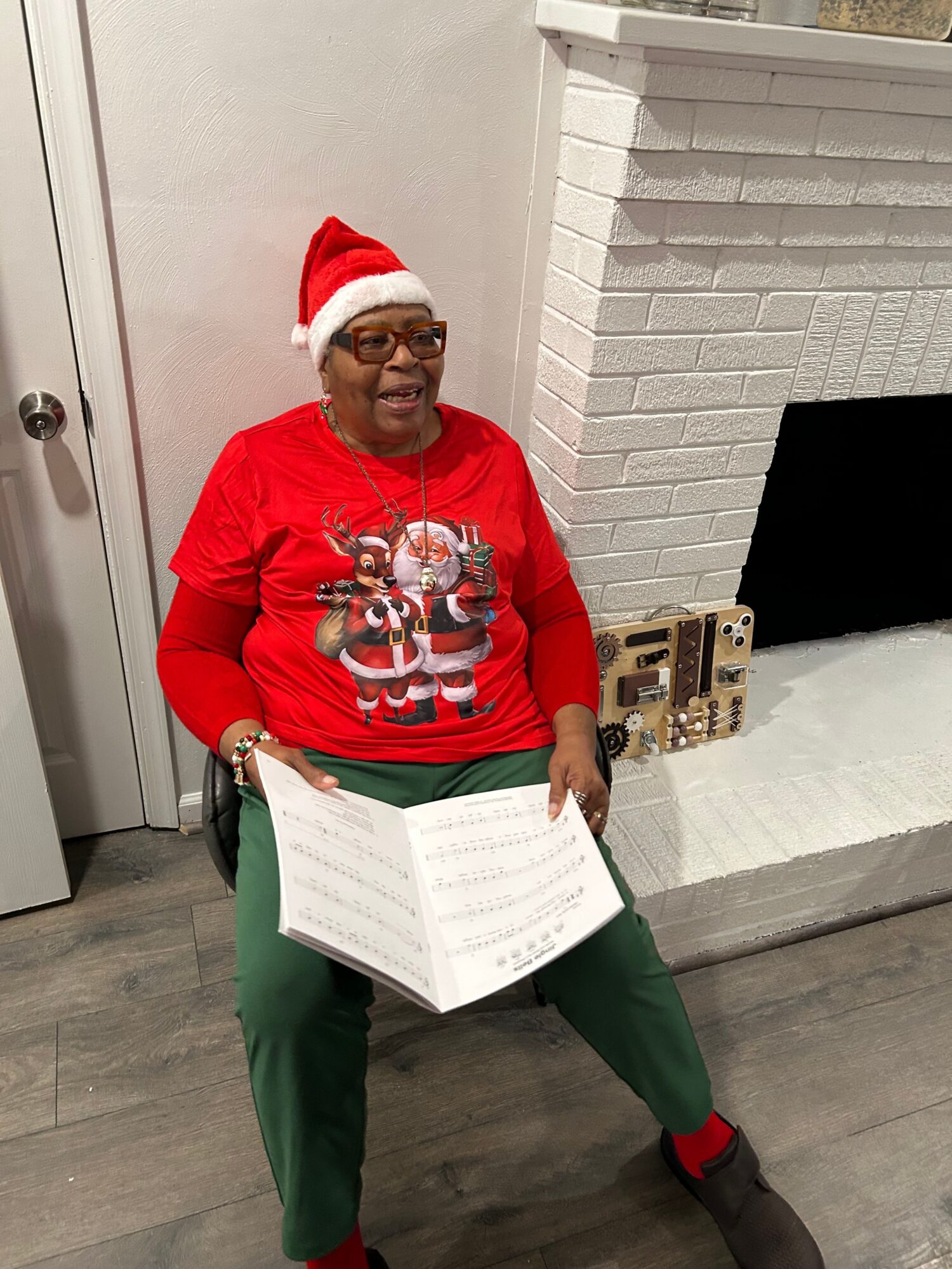 Person wearing a Santa hat and red sweater with a Christmas design, sitting on the floor, reading a large book.