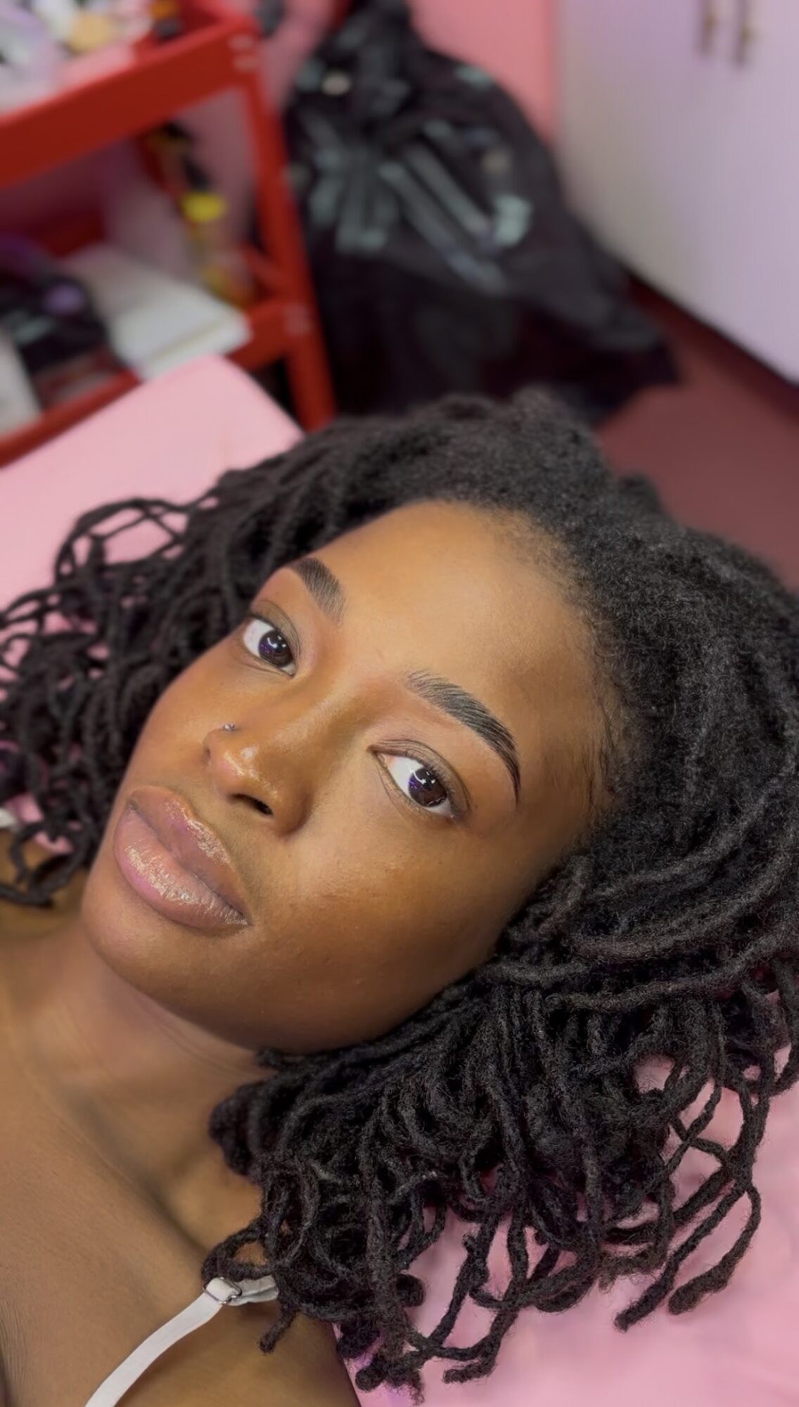 Close-up of a woman with natural curly hair lying down, looking at the camera, with a blurred background.