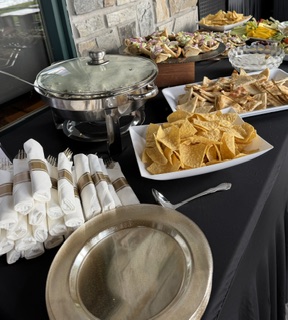 Buffet table with chips, snacks, and a covered chafing dish, set against a stone wall background.