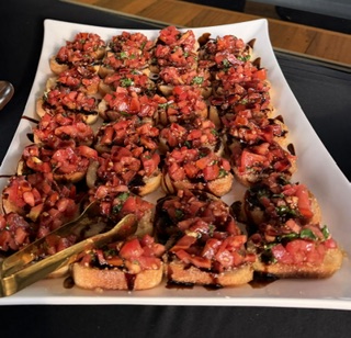 Tray of sliced bread topped with chopped tomatoes, herbs, and other ingredients, garnished with green herbs, on a white paper-lined tray.