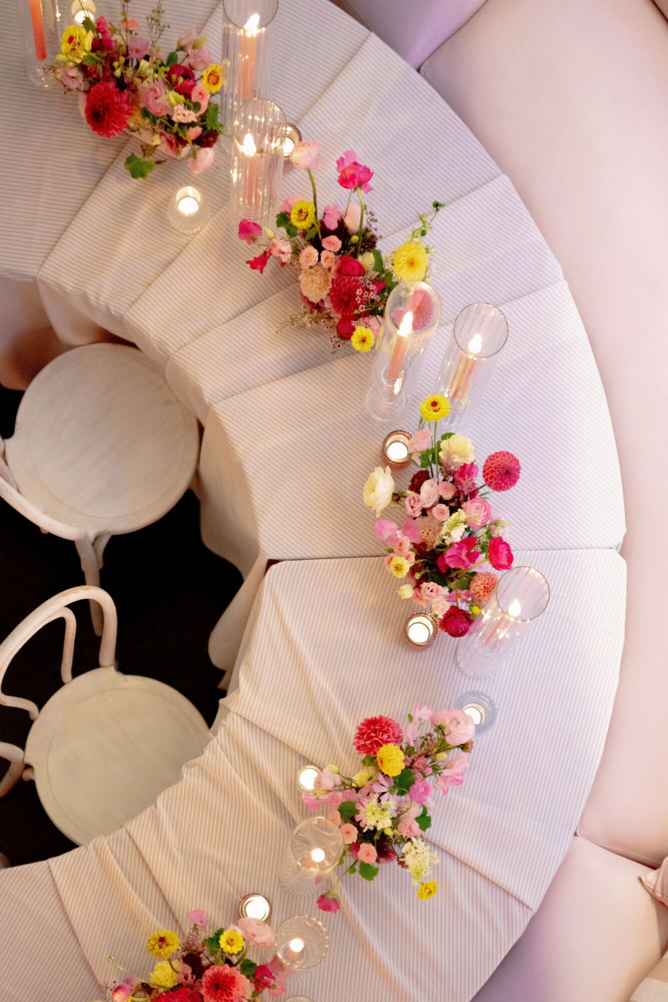 Decorative circular table with floral arrangements and candles, surrounded by chairs, viewed from above.