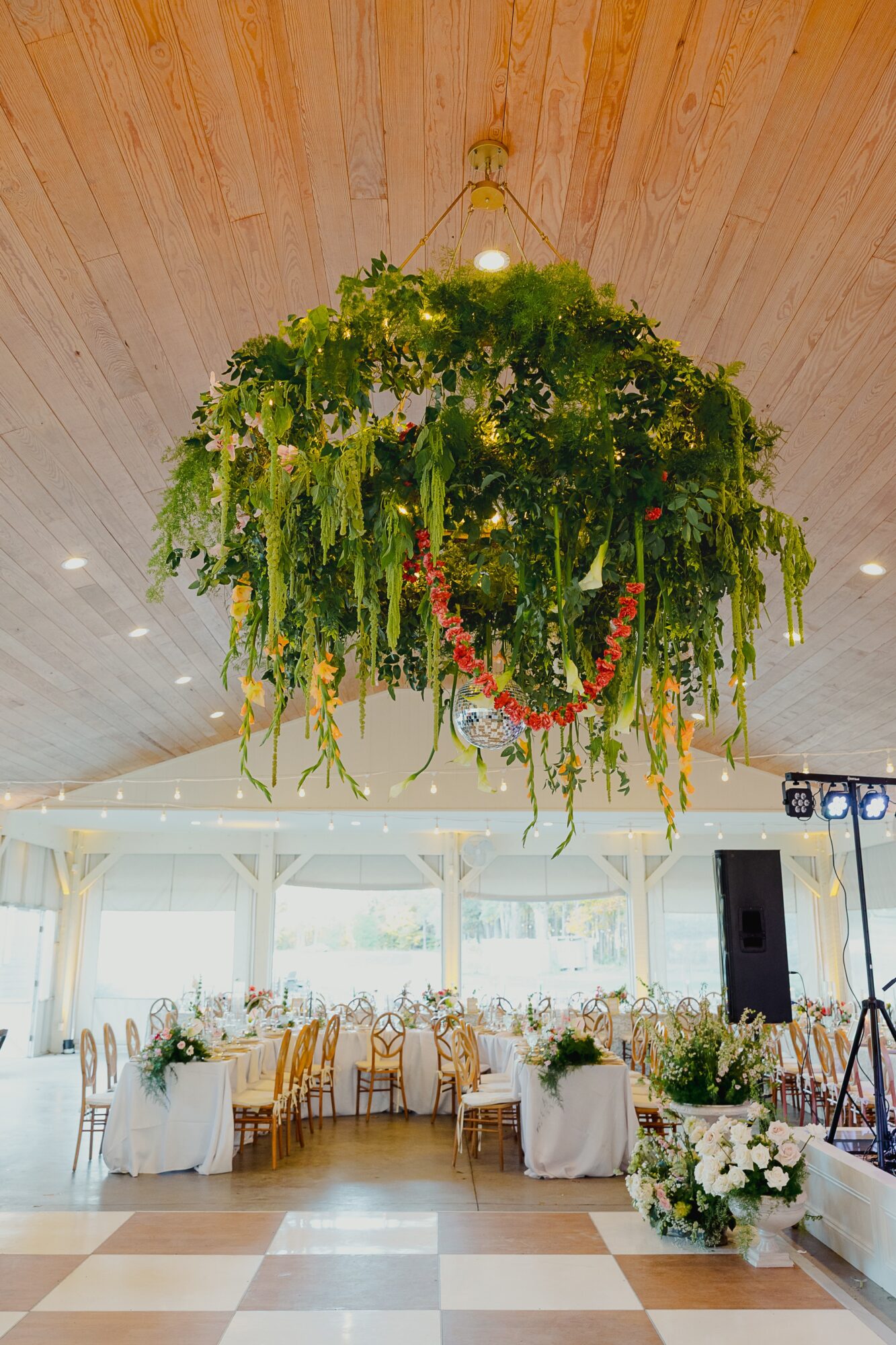 Large hanging floral arrangement with green foliage and hanging flowers above banquet tables in a decorated event space.