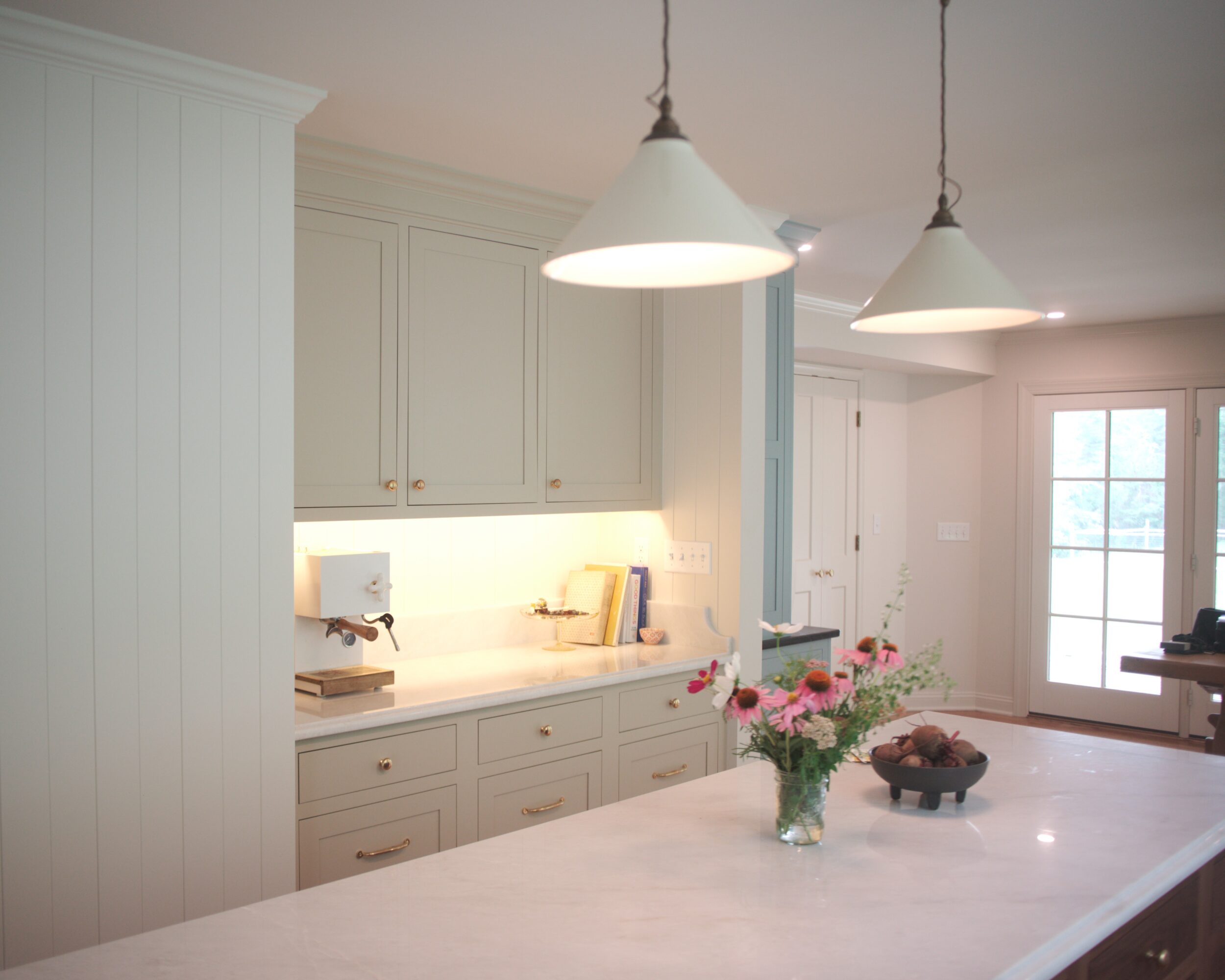Kitchen with white cabinets, pendant lights, and a countertop with a vase of pink flowers.