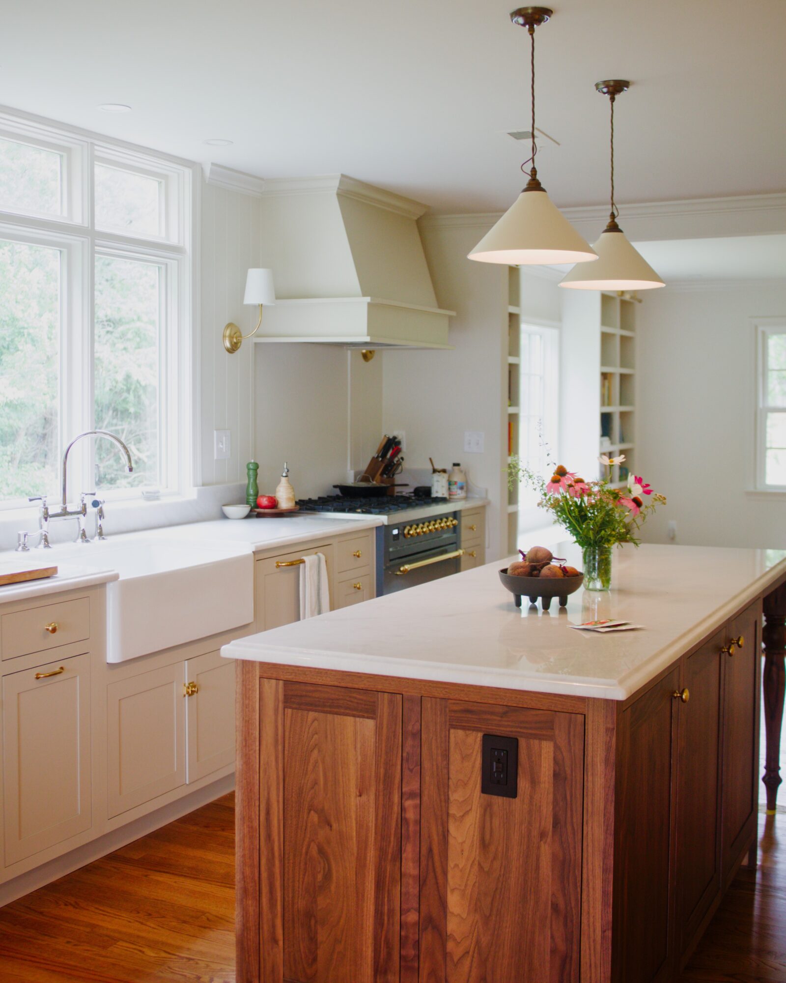 Kitchen with white cabinets, a large window, a white countertop, and a wooden island with a vase of flowers, pendant lights, and a stove.