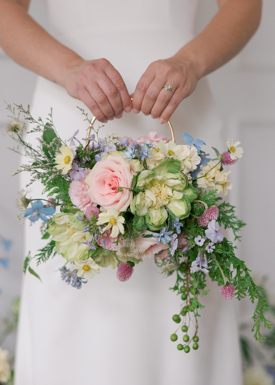Person holding a colorful flower bouquet with pink, white, purple, and green flowers and foliage, wearing a white dress.