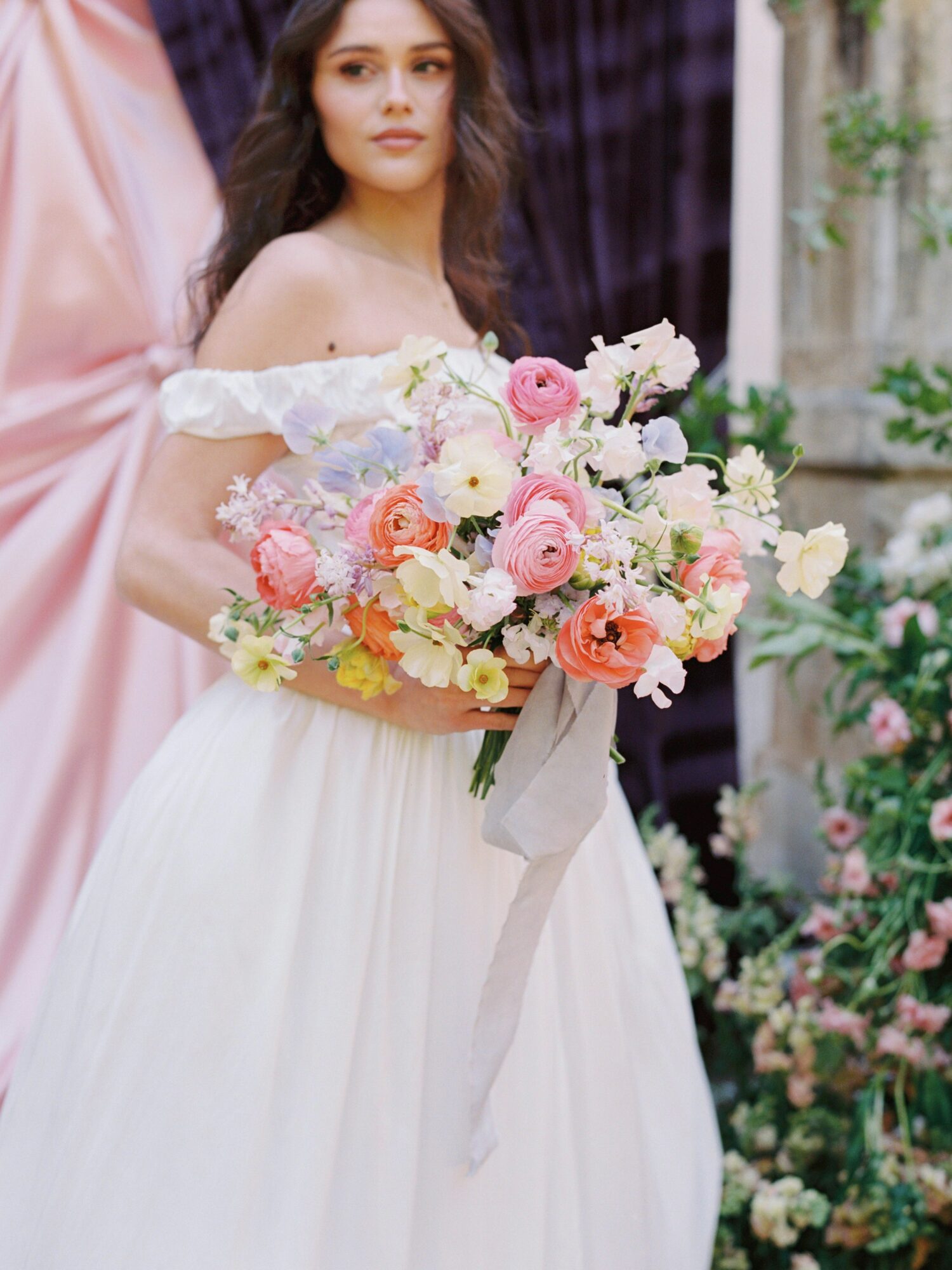 Young woman in wedding dress holding a large bouquet of pink, white, and peach flowers, standing outdoors.