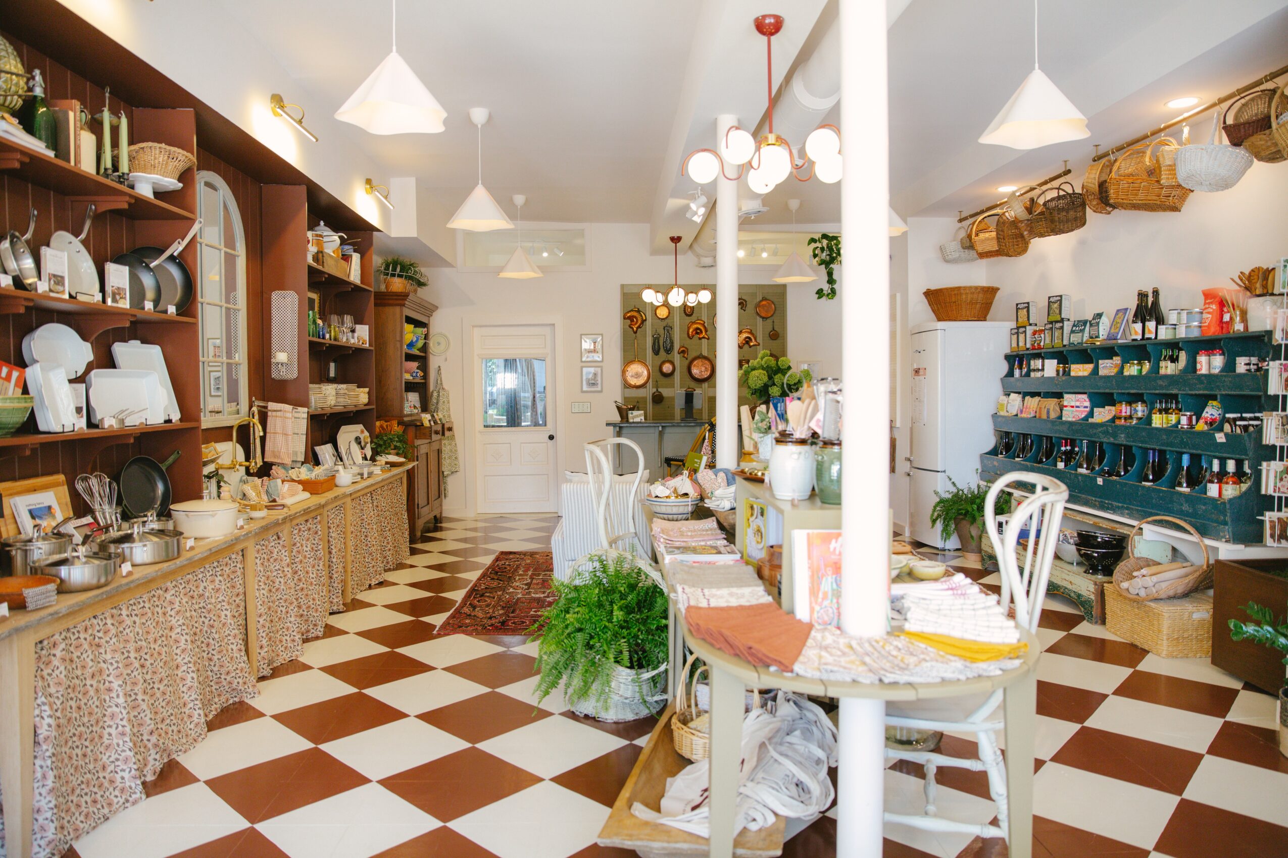 Interior of a cozy shop with shelves of dishes, cups, and kitchenware, checkered floor, and bright lighting.
