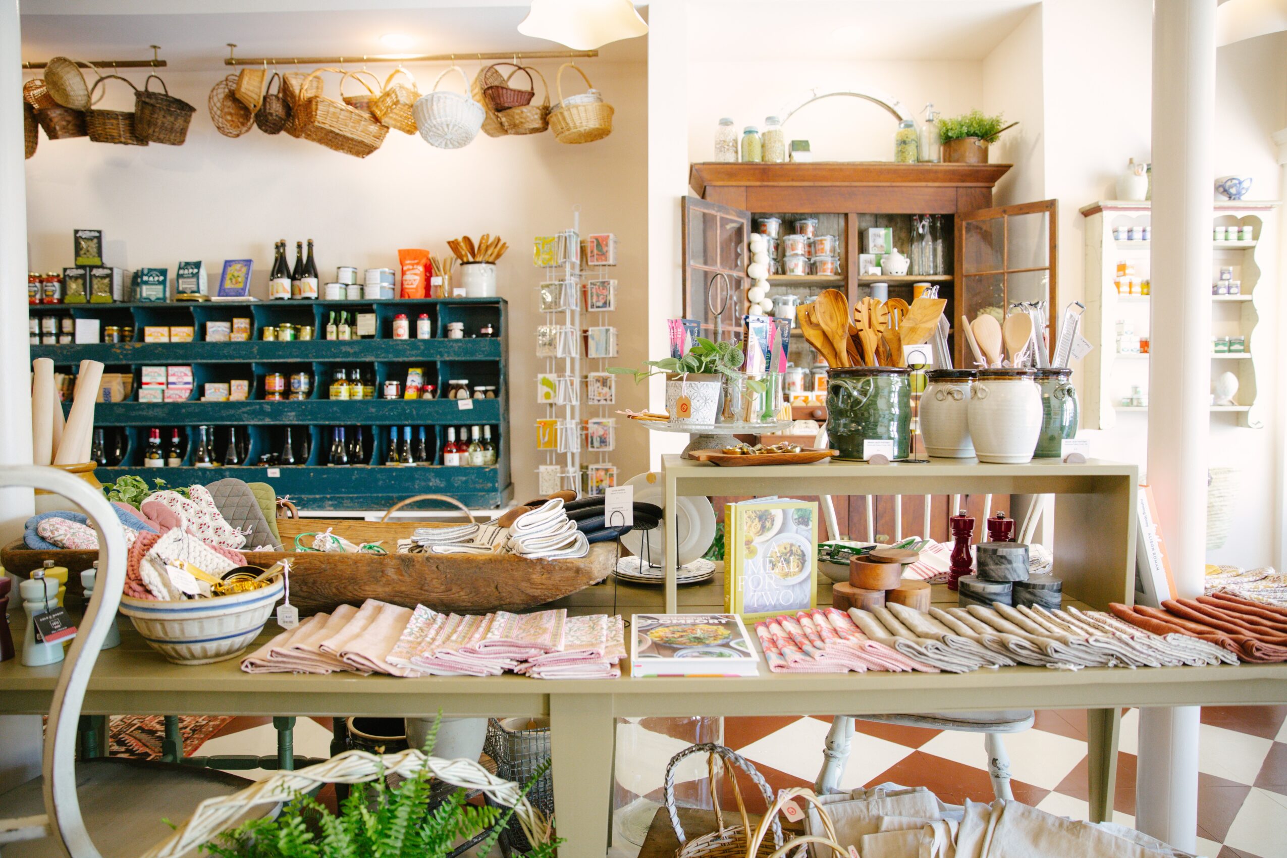 Interior of a cozy shop with shelves of kitchenware, baskets, and a table with various items, bright and inviting.