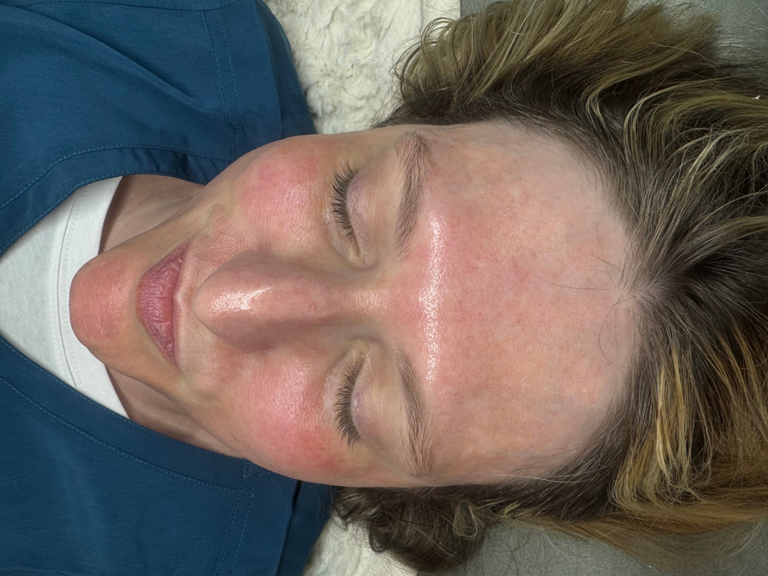 Close-up of a woman with closed eyes and light brown hair lying down, wearing a blue top.