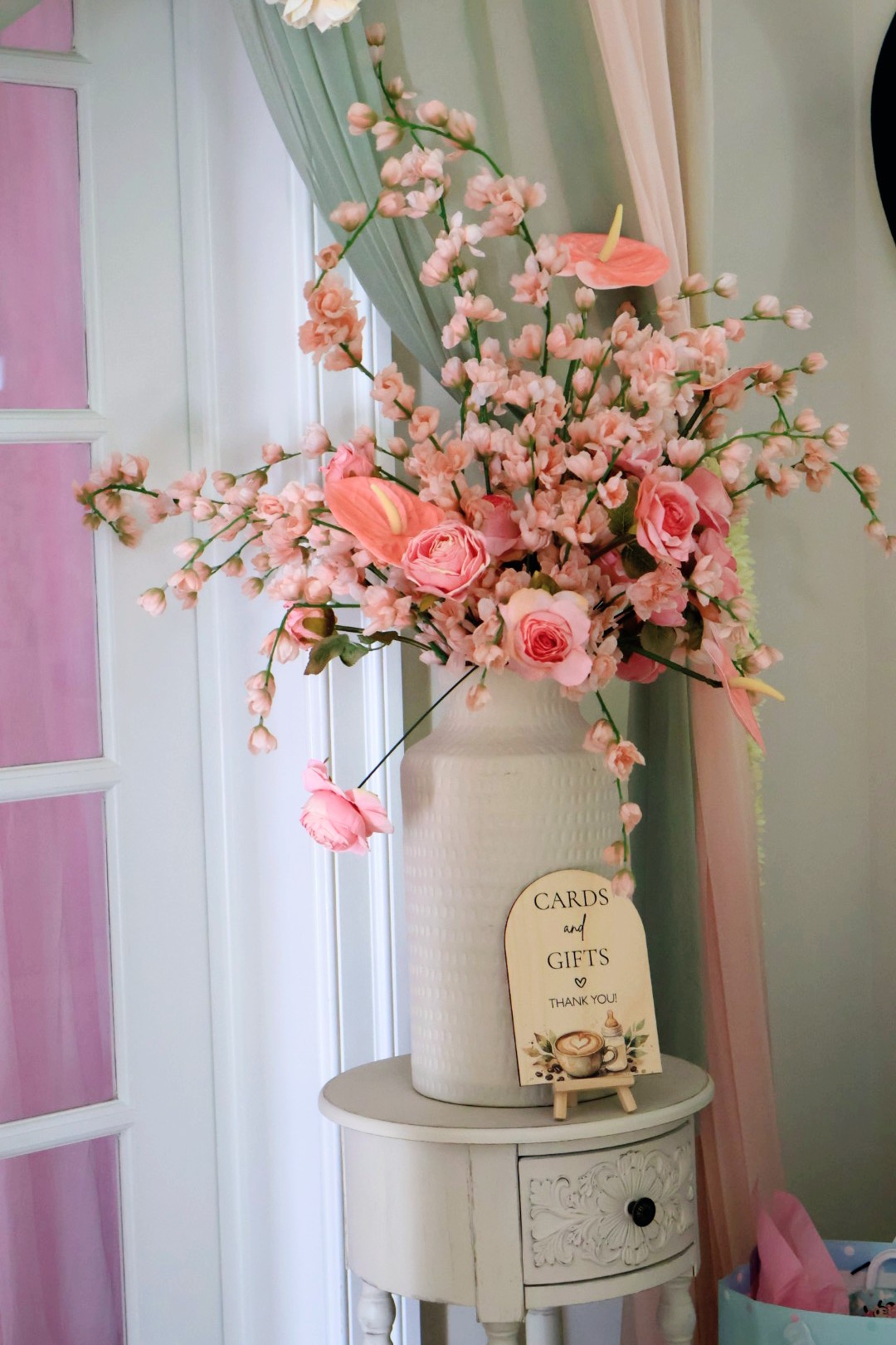 Pink and white flowers in a white vase on a small table, with a gift card and a pink umbrella decoration.