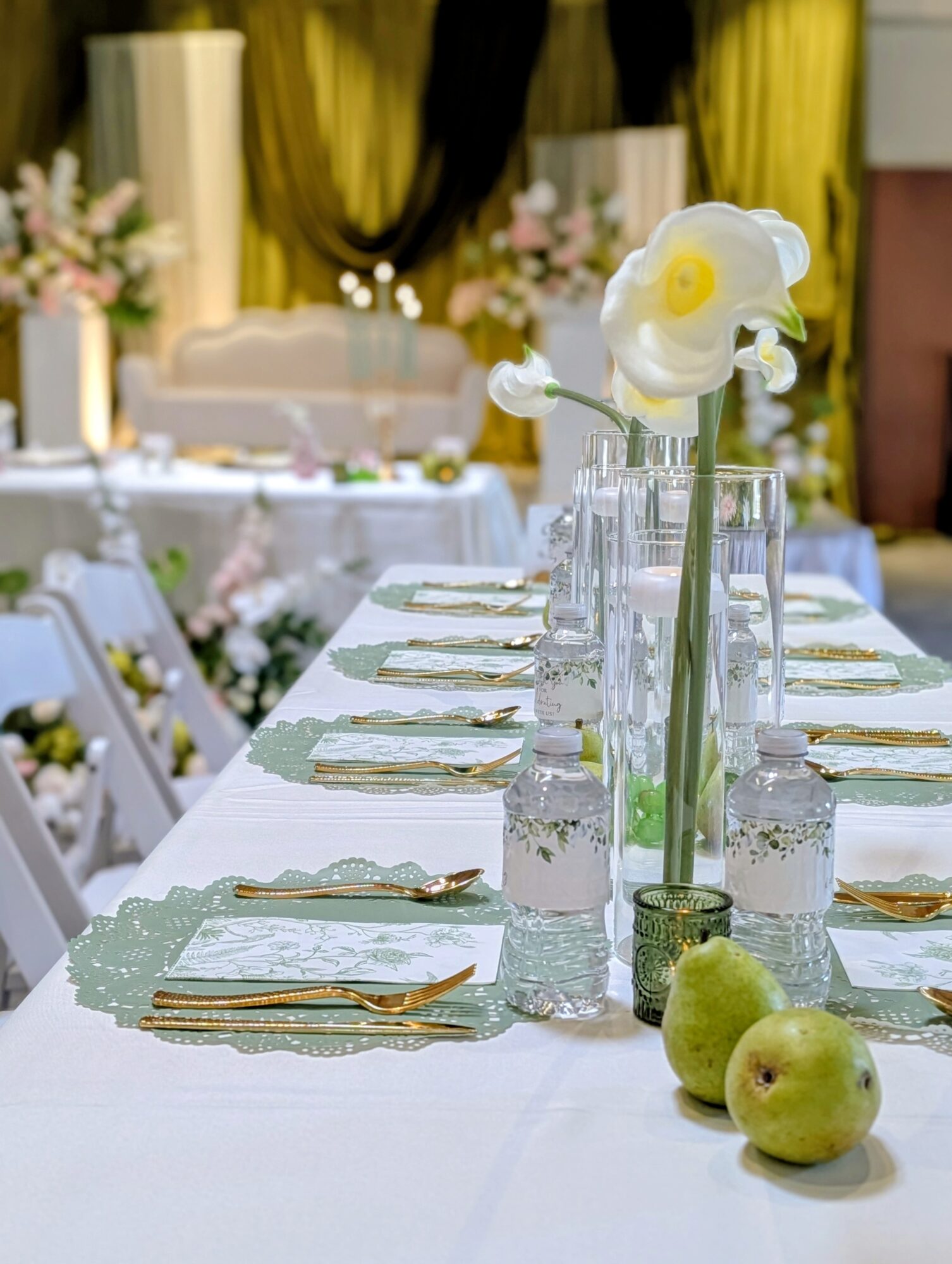 Table set with plates, cutlery, water bottles, and a tall vase with white flowers, in a decorated event space.
