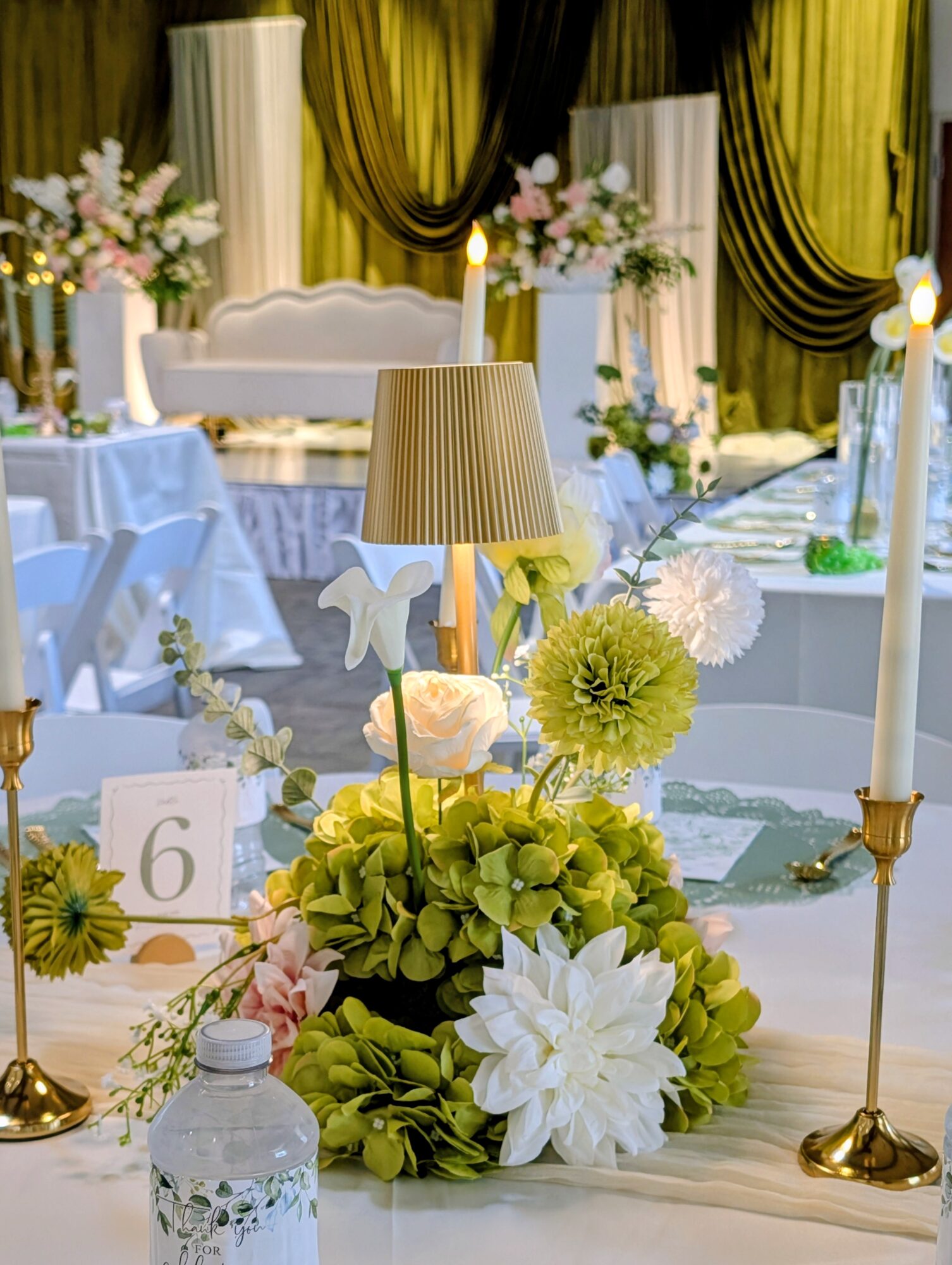 Decorated table with flowers, candles, a lamp, and a table number, set for an event or celebration.