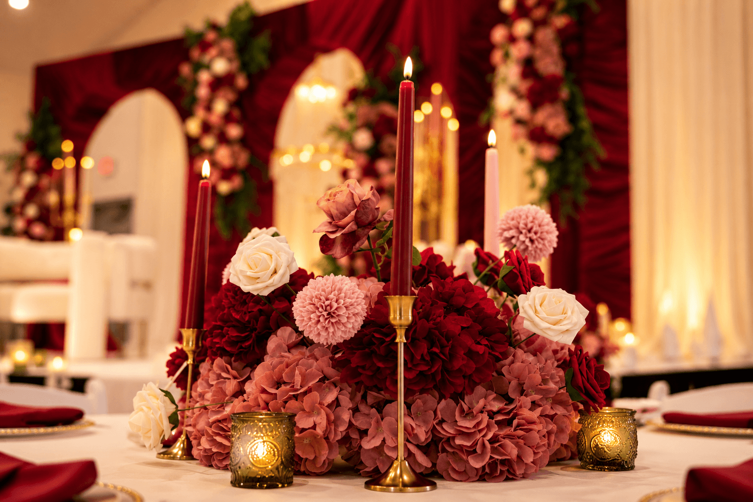 Elegant floral centerpiece with pink and white roses, red and pink hydrangeas, and tall red candles on a decorated table.