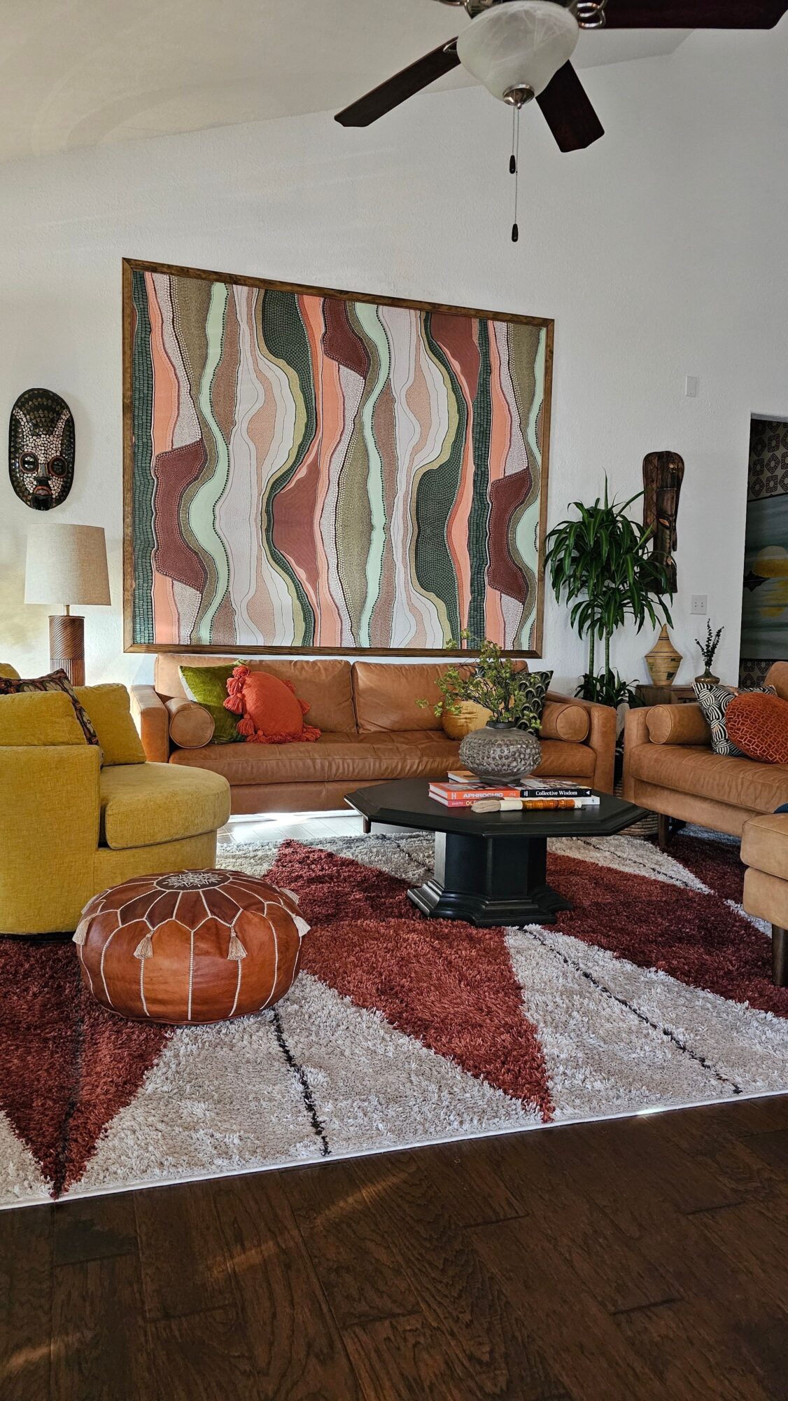 Living room with colorful abstract wall art, yellow armchair, patterned rug, and decorative items on a wooden floor.