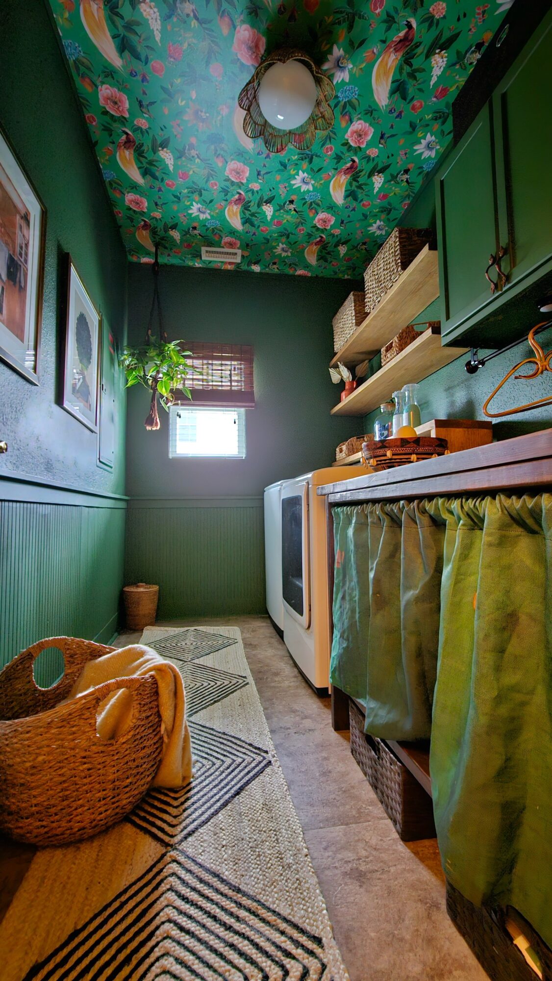 Laundry room with green walls, floral ceiling, window, shelves, washing machine, and a basket on a patterned rug.