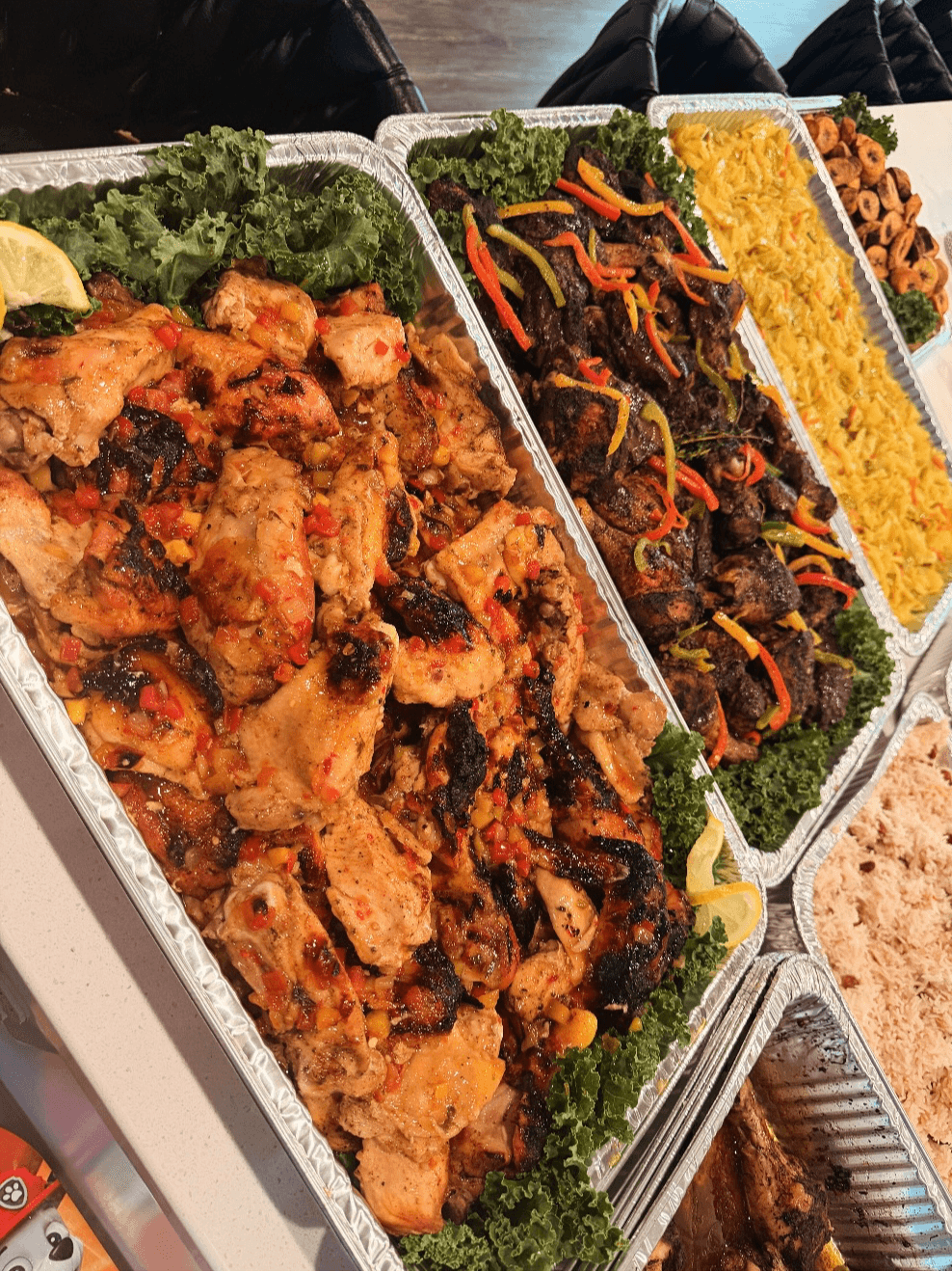 Three trays of food with fried chicken, stir-fried vegetables, and rice, garnished with greens, on a table.