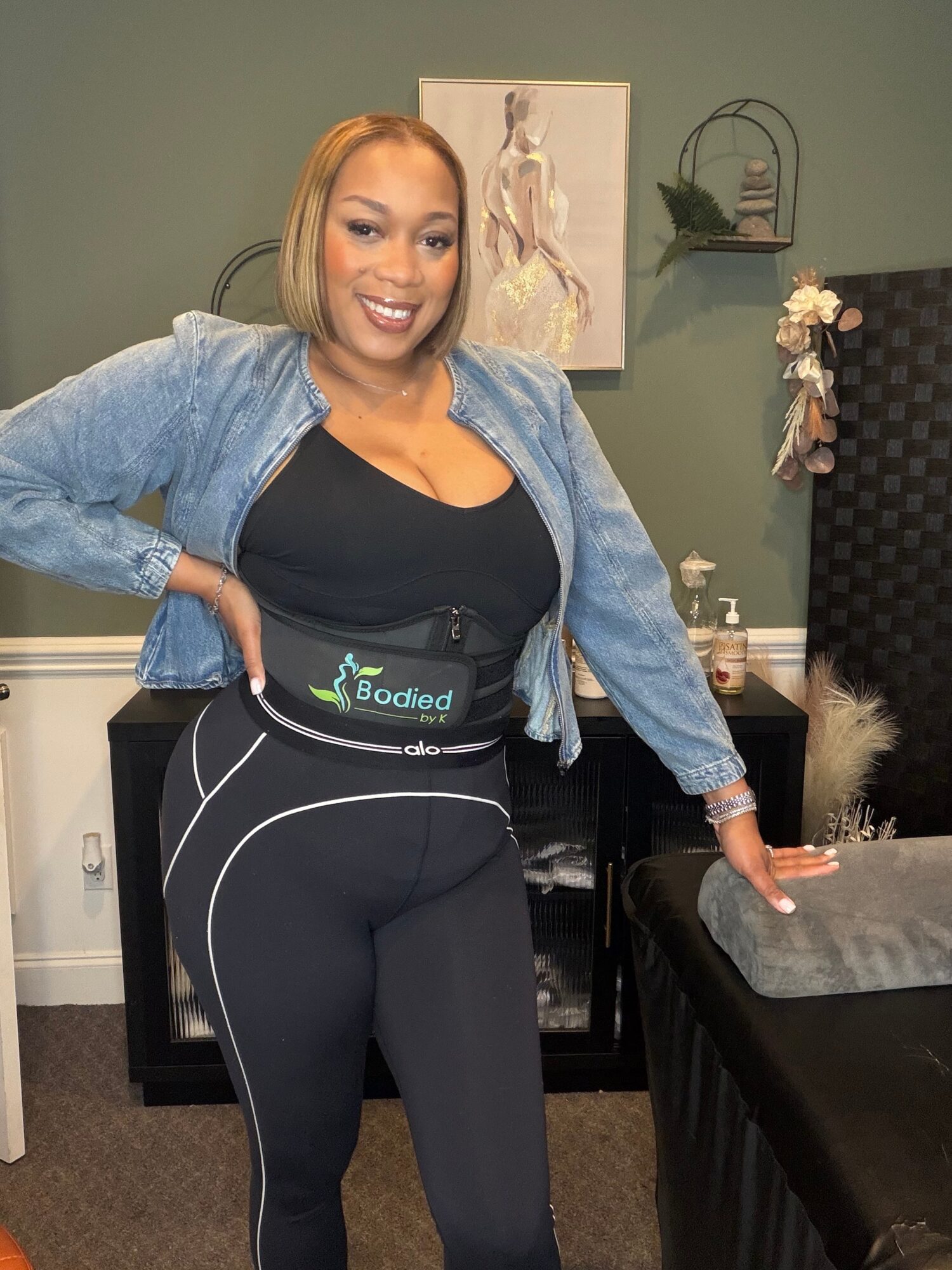 Woman smiling, wearing a waist belt, standing in a room with artwork and furniture.