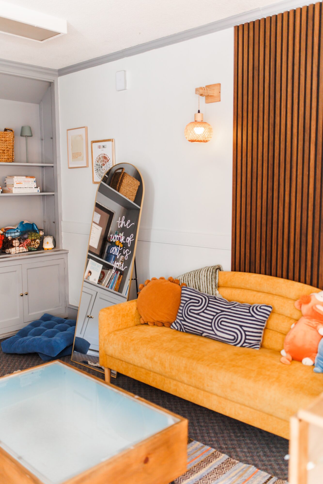 Living room with orange sofa, striped pillow, wall-mounted light, mirror, and bookshelf, with wooden paneling on the wall.