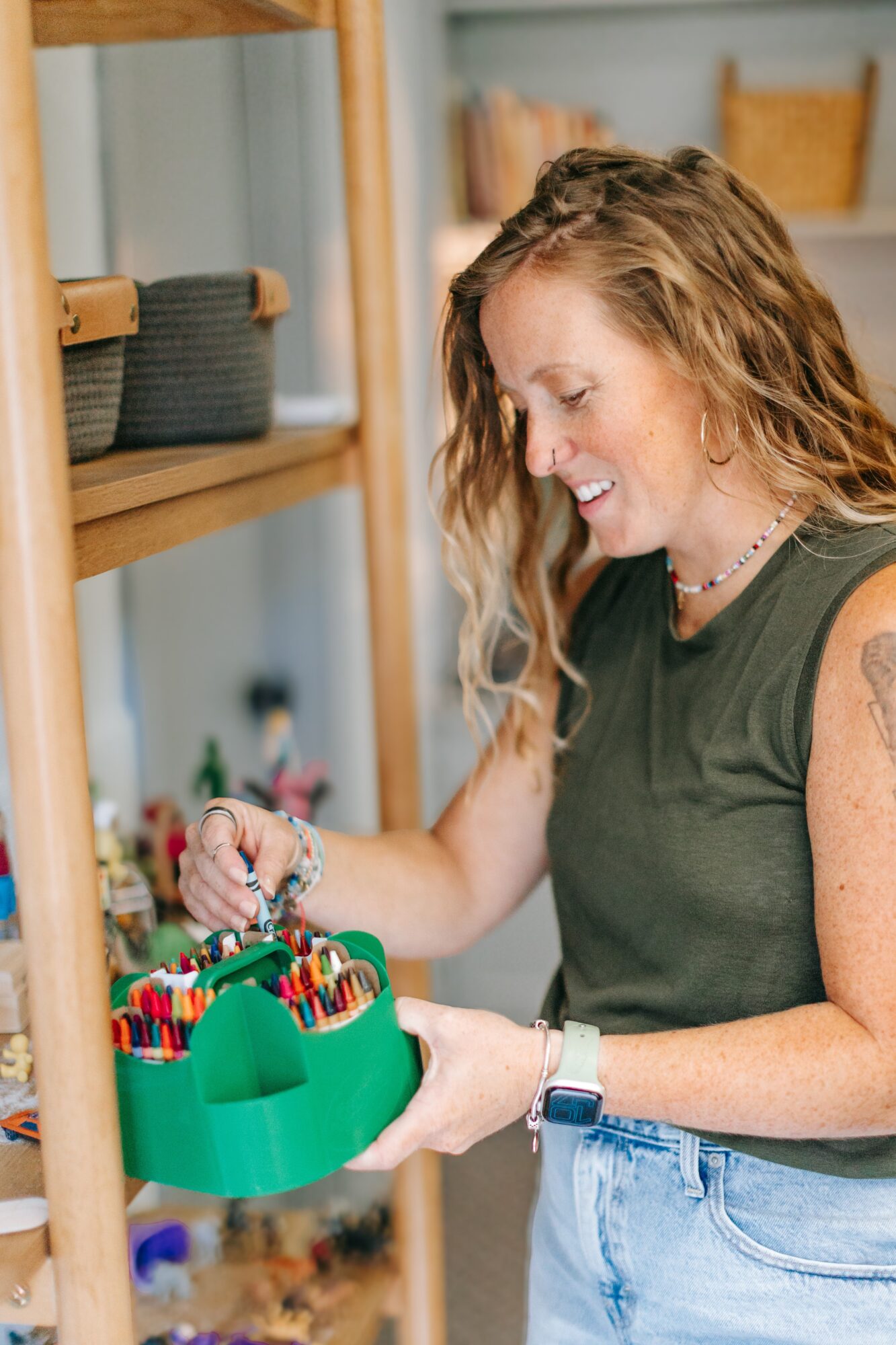 Woman with curly hair looking at a green container of colorful pens on a shelf.
