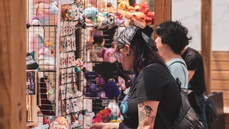 Two women browse yarn and knitting supplies at a store, with shelves filled with colorful yarns and knitting accessories.