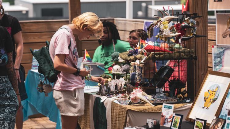 People browsing a market stall with various items on display, including framed pictures and decorative objects.