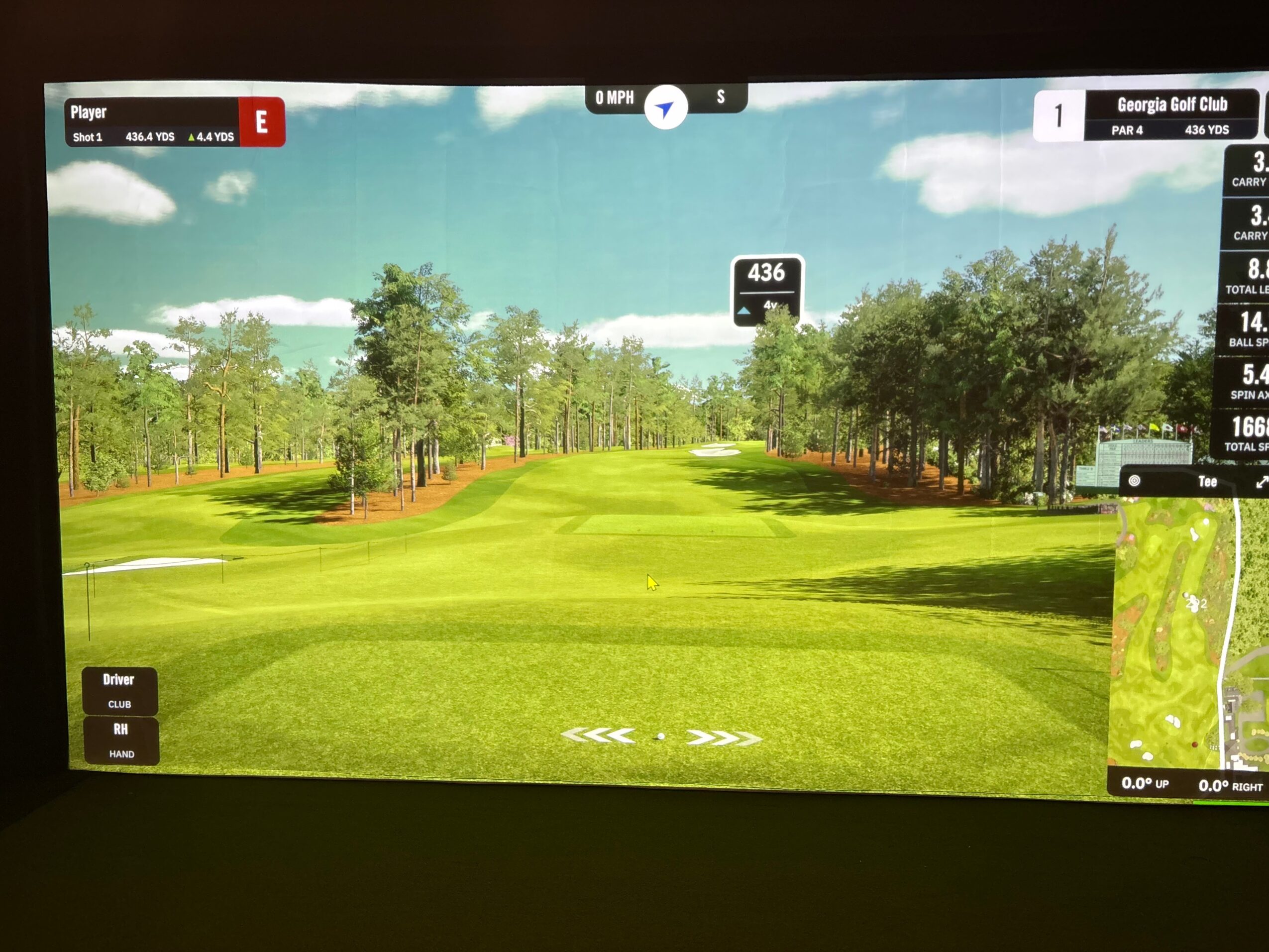Golf course with green fairway, trees, and blue sky, displayed on a screen with game information and a small map.