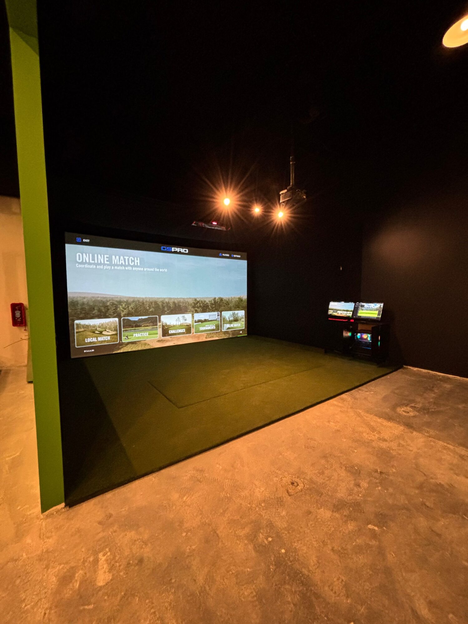 Indoor space with a large screen displaying a presentation, green and concrete flooring, and dark walls.