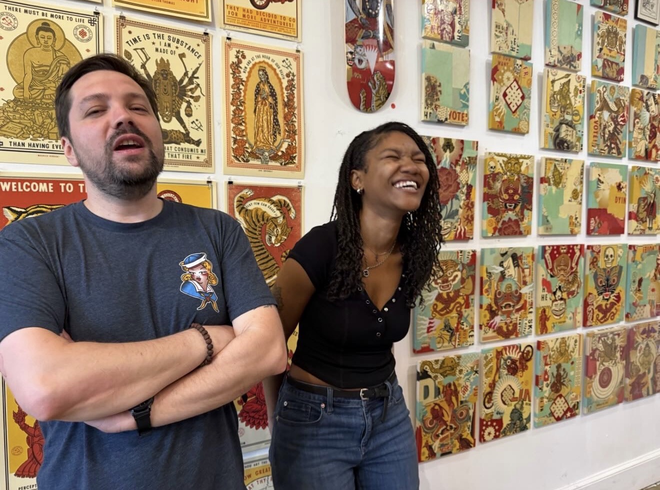 Two people smiling and standing in front of colorful artwork on a wall.