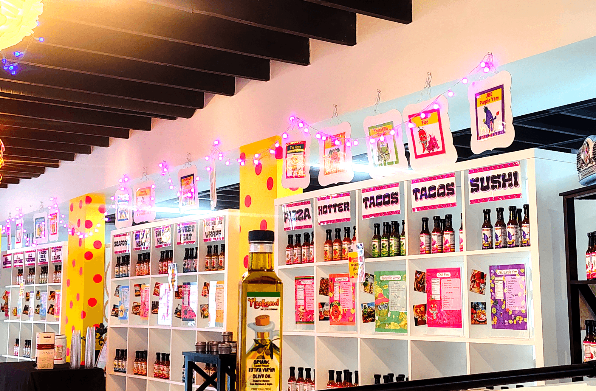 Display shelves with colorful packaging and bottles, decorated with pink string lights, in a brightly lit store interior.