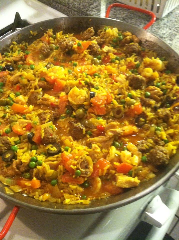 Large pan of cooked rice with vegetables and meat, including carrots, peas, and corn, on a stovetop.
