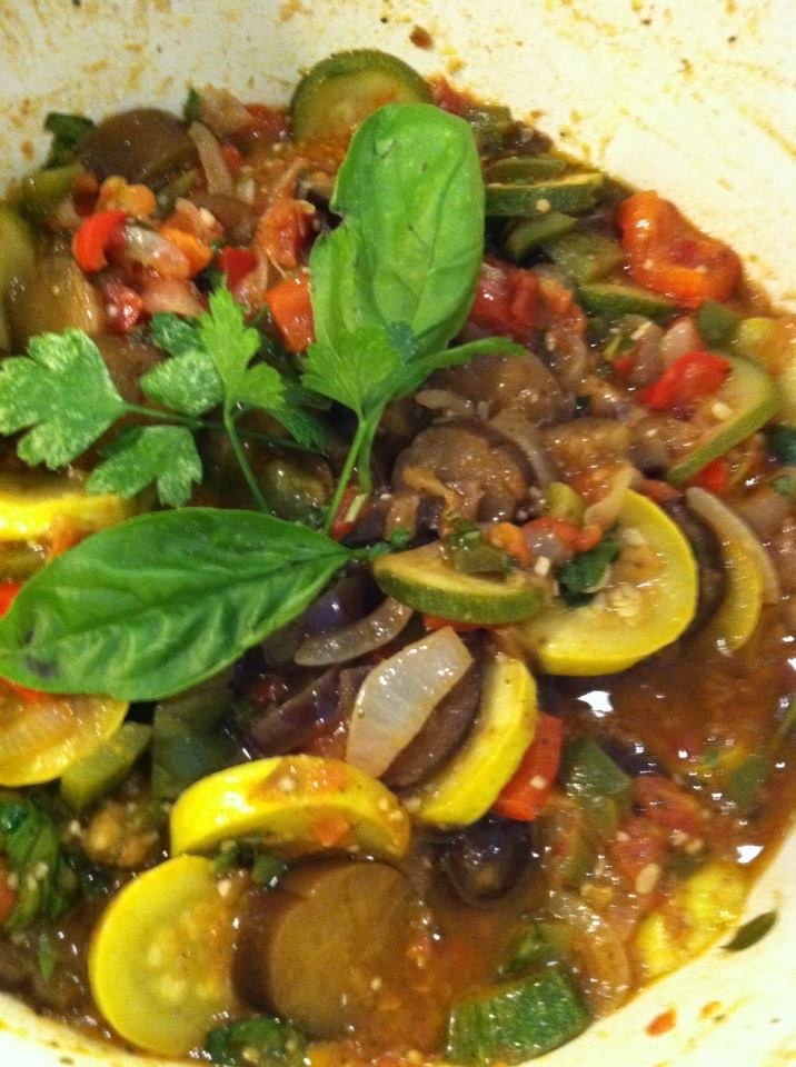 Close-up of a vegetable dish with zucchini, eggplant, tomatoes, onions, and fresh herbs, garnished with basil and cilantro leaves.