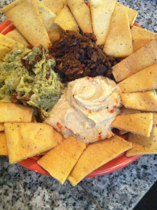 Plate with tortilla chips, guacamole, sour cream, and a dark meat dish, on a speckled countertop.