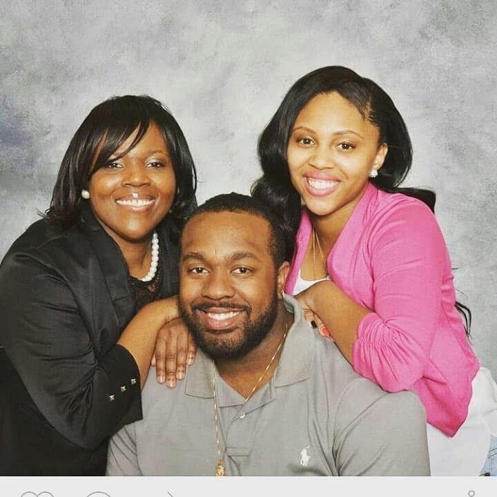 Three people smiling, two women and one man, posing together against a gray background.