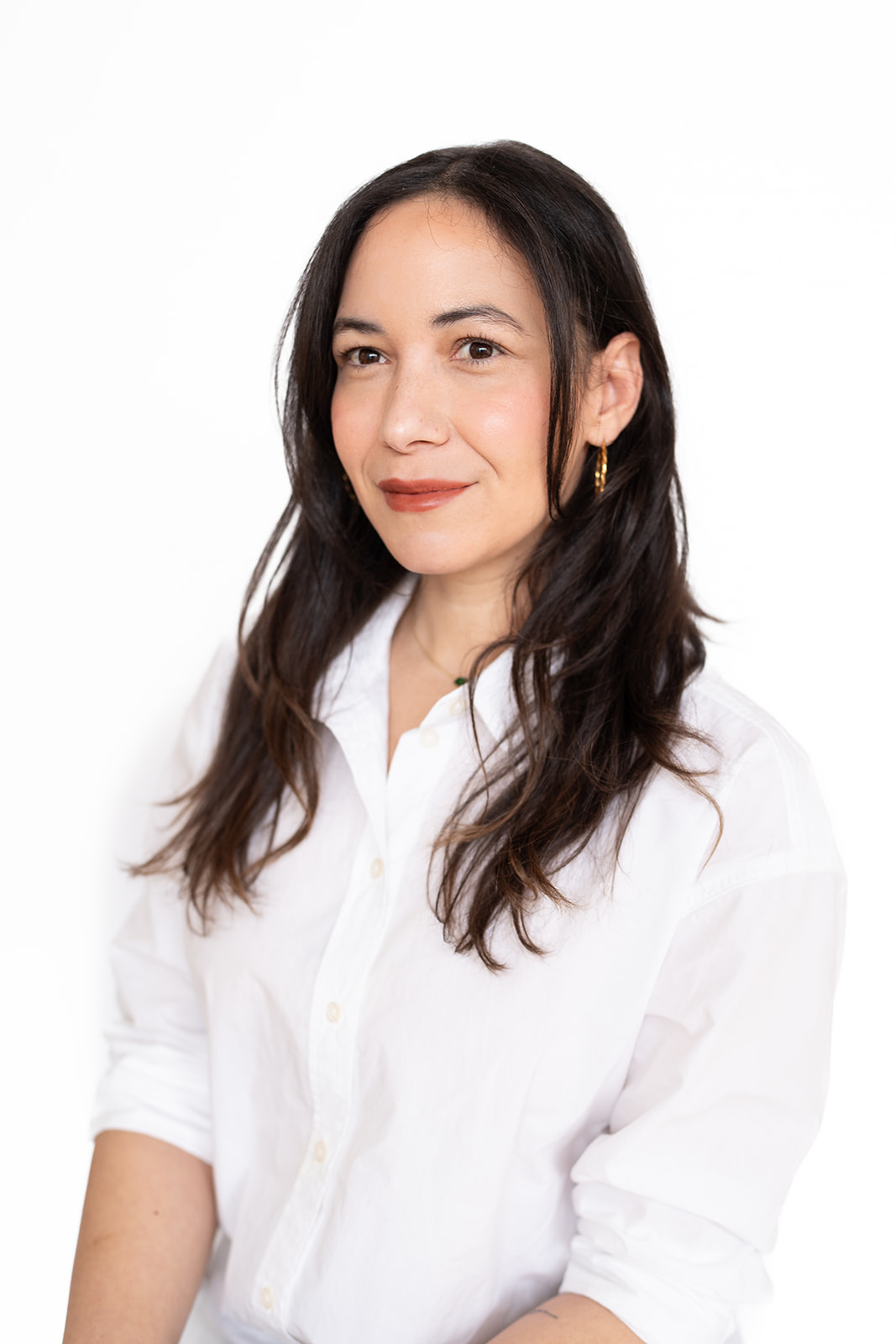 Woman with long dark hair wearing a white shirt, smiling, against a white background.