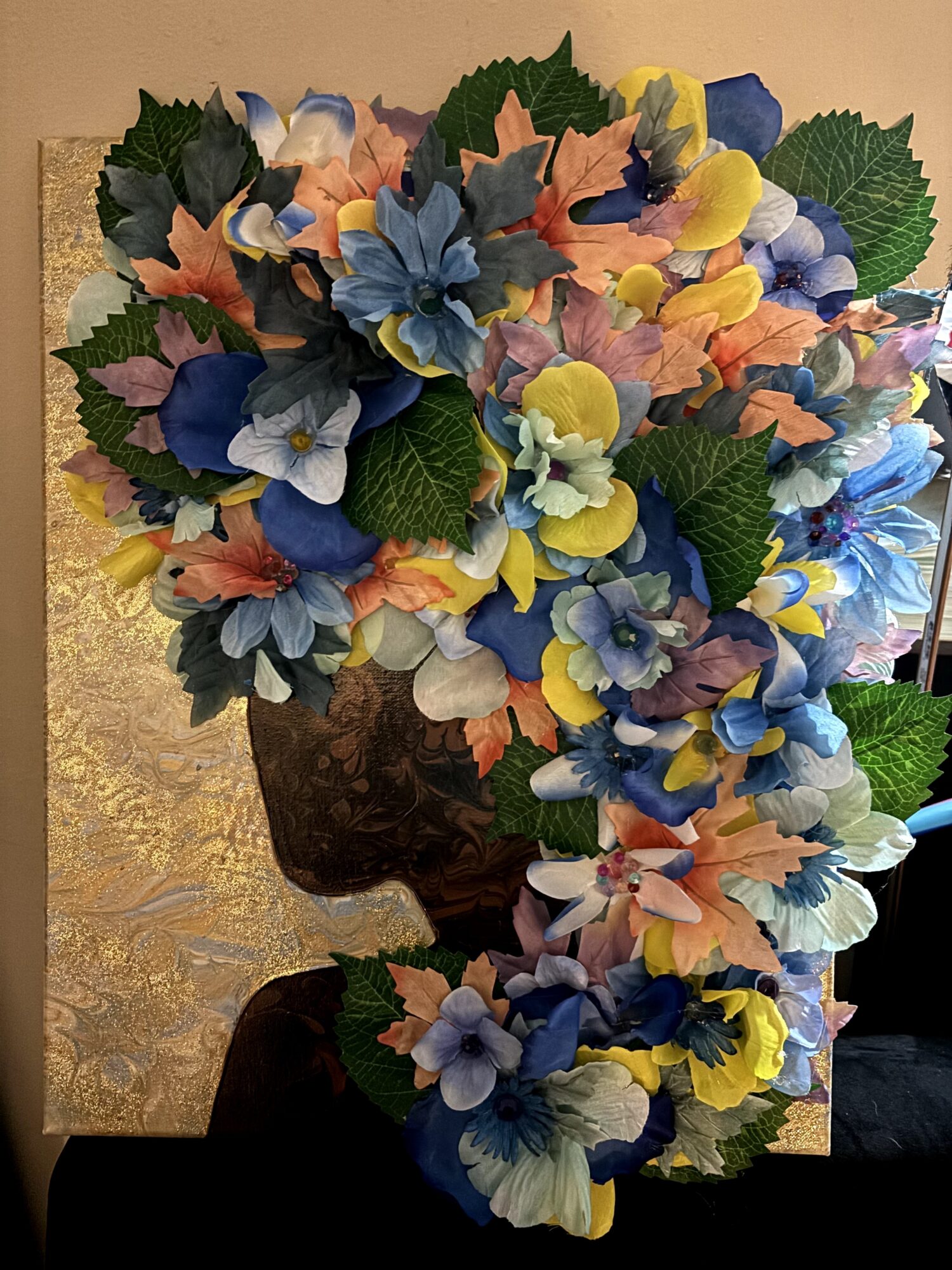 A collage of colorful flowers arranged to resemble a person's head and hair, with green leaves and a dark background.