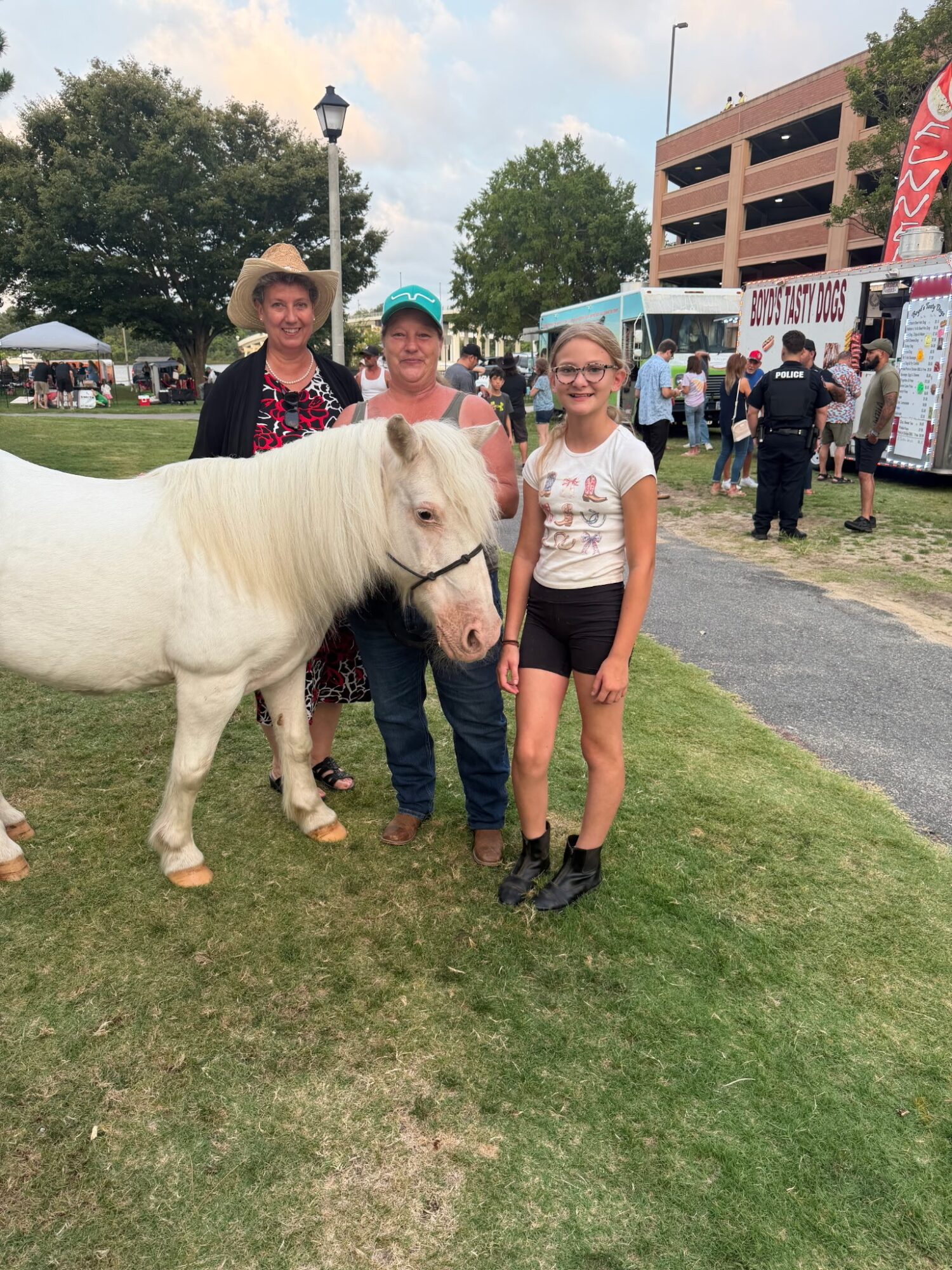 Three people stand beside a small white horse at an outdoor event.
