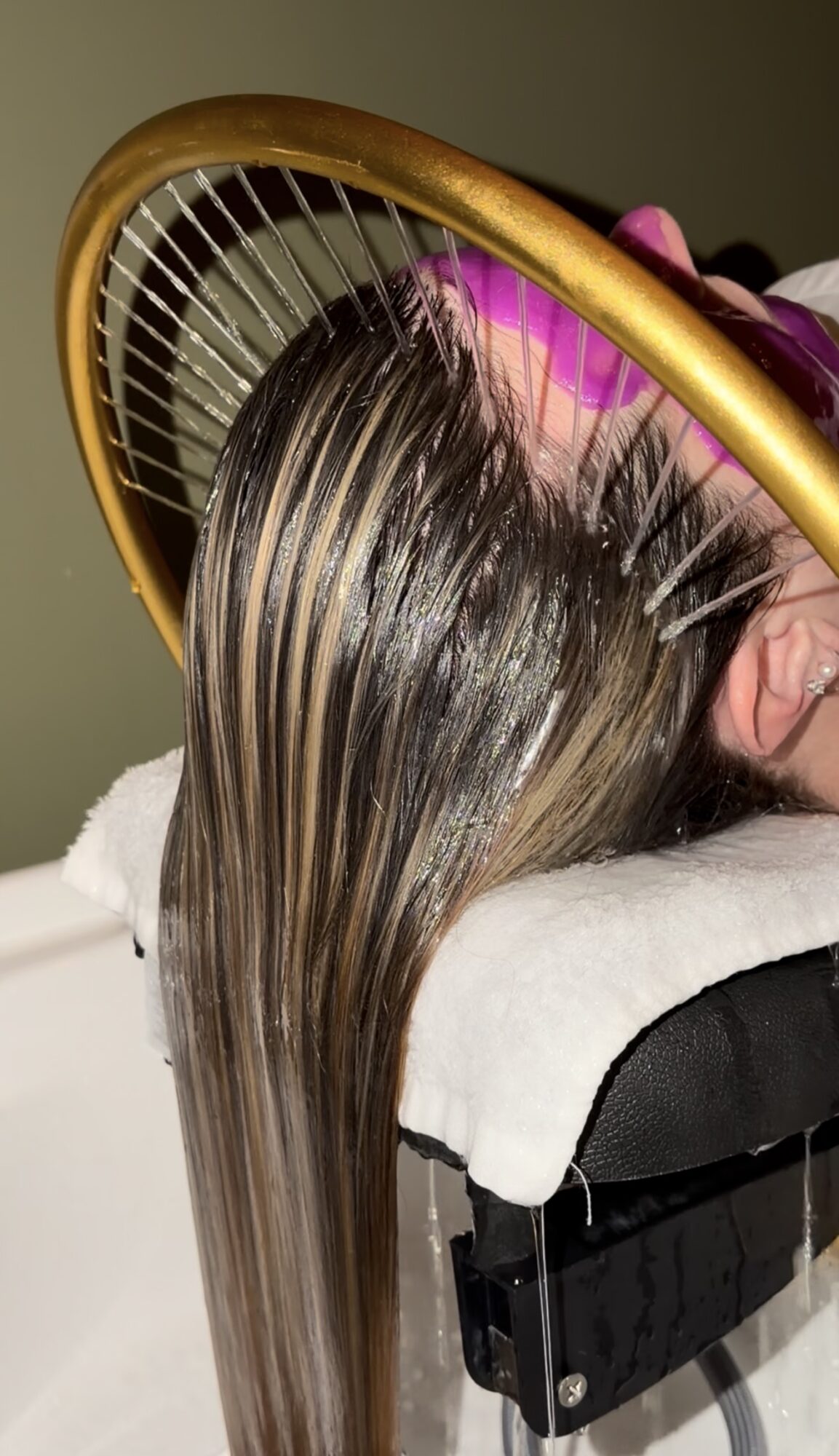Person's hair is being dried with a round hairbrush and hairdryer, hair appears wet and shiny.