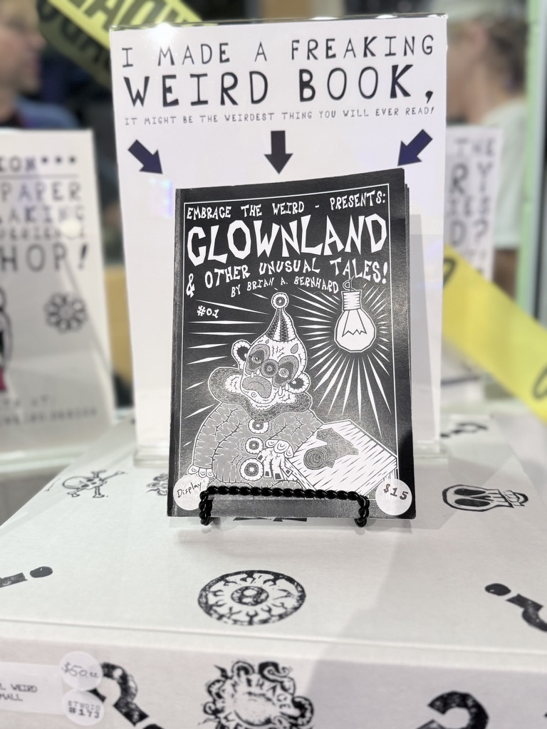 Book display with a sign reading 'Freaking Weird Book' and a black-and-white illustration of a clown with a hat and bow tie.