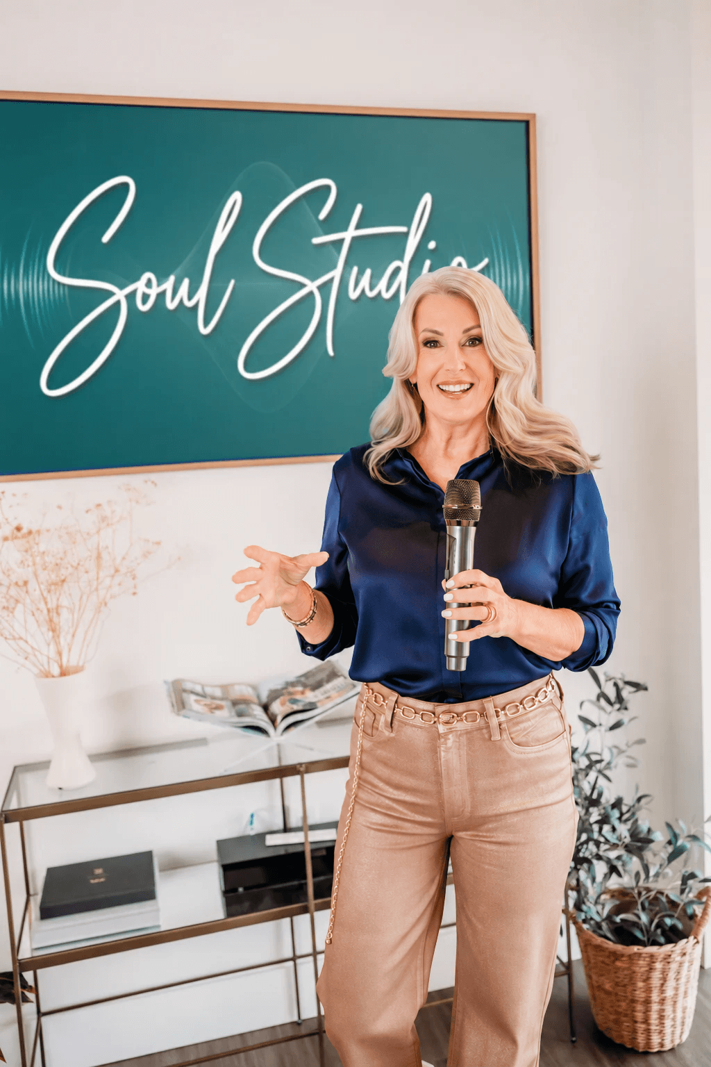 Woman with blonde hair holding a microphone, smiling, standing in front of a green sign that reads 'Soul Studio'.