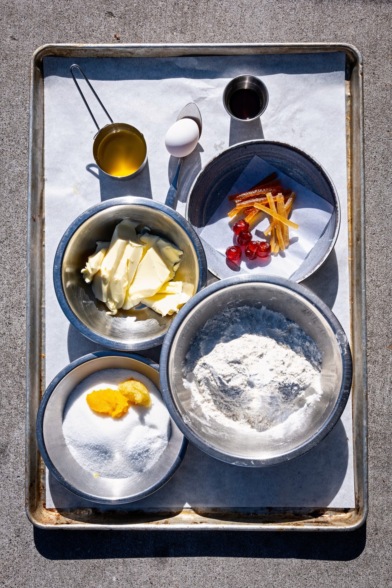 Baking ingredients on a tray, including flour, eggs, butter, and toppings, with measuring spoons and bowls.