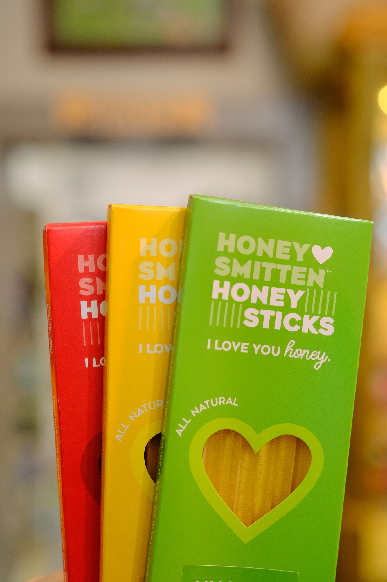 Three boxes of honey sticks in red, yellow, and green, displayed on a blurred background.