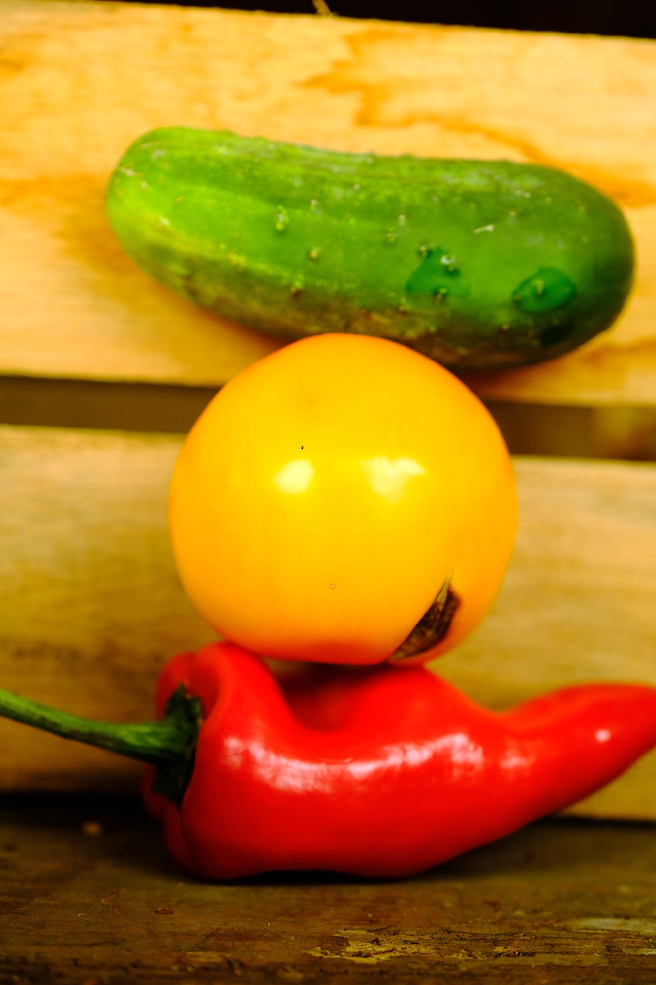 Cucumber, yellow tomato, and red chili pepper on wooden surface.