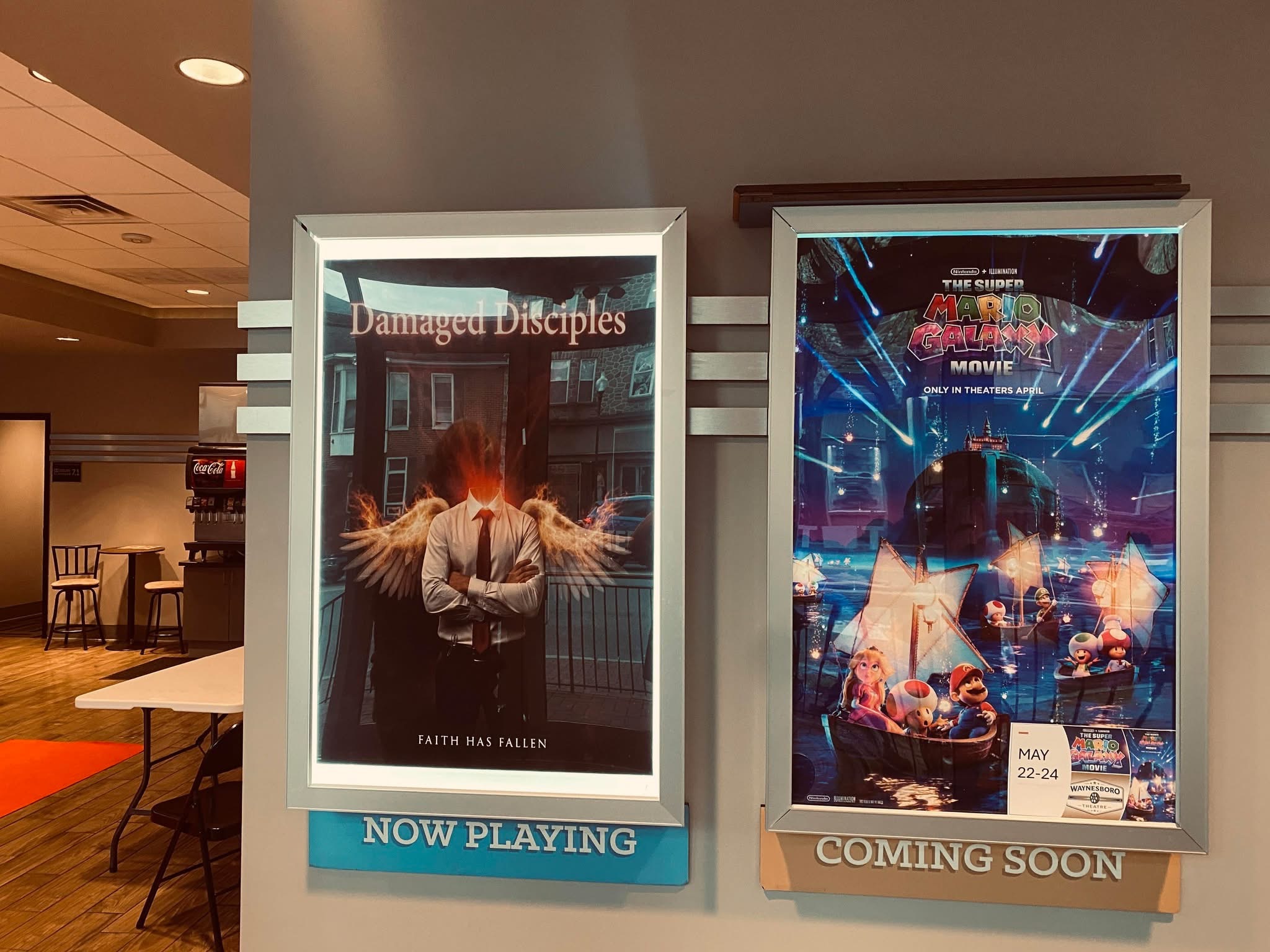 Two digital screens display event posters; one shows a person with wings, the other shows a DJ at a concert.