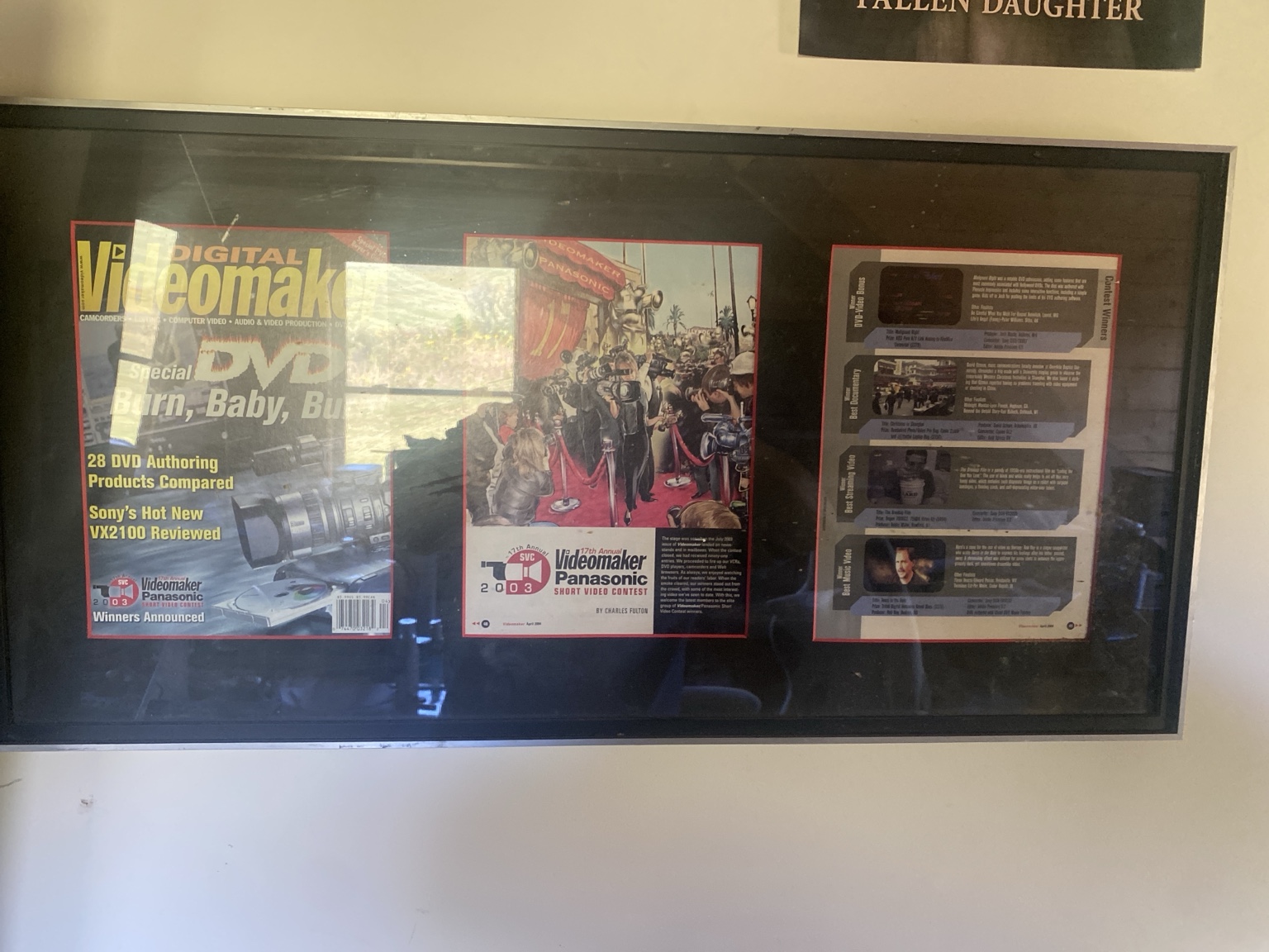Display case with magazines and DVDs, some with colorful covers and text, reflected on glass surface.