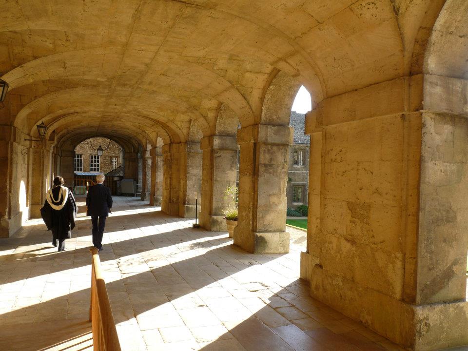 Three people walk under a stone archway with sunlight casting shadows on the ground.