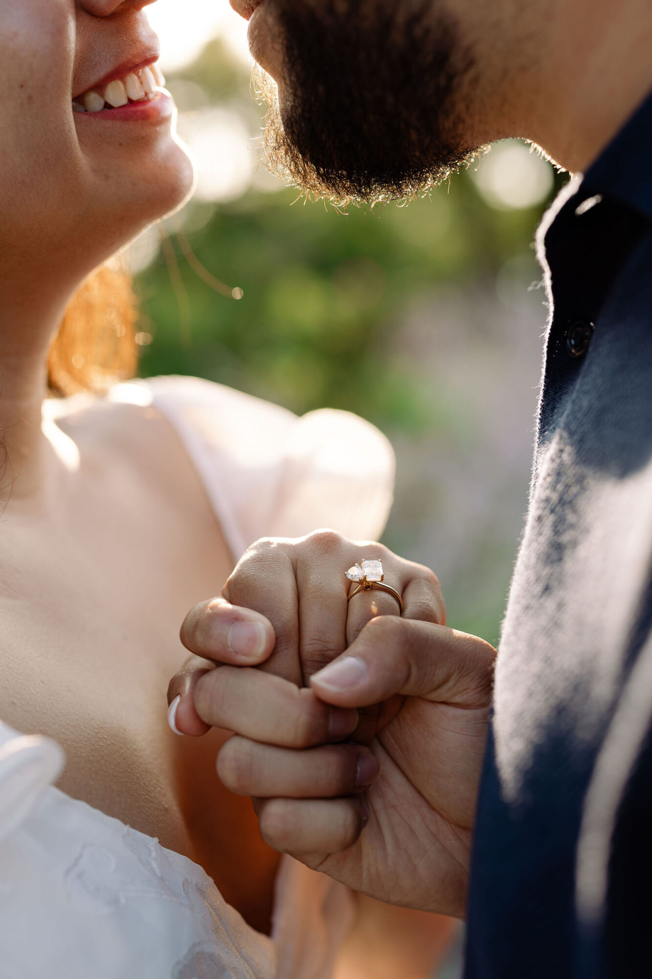 Close-up of a couple holding hands, with a woman smiling and a man with a beard, outdoors background.